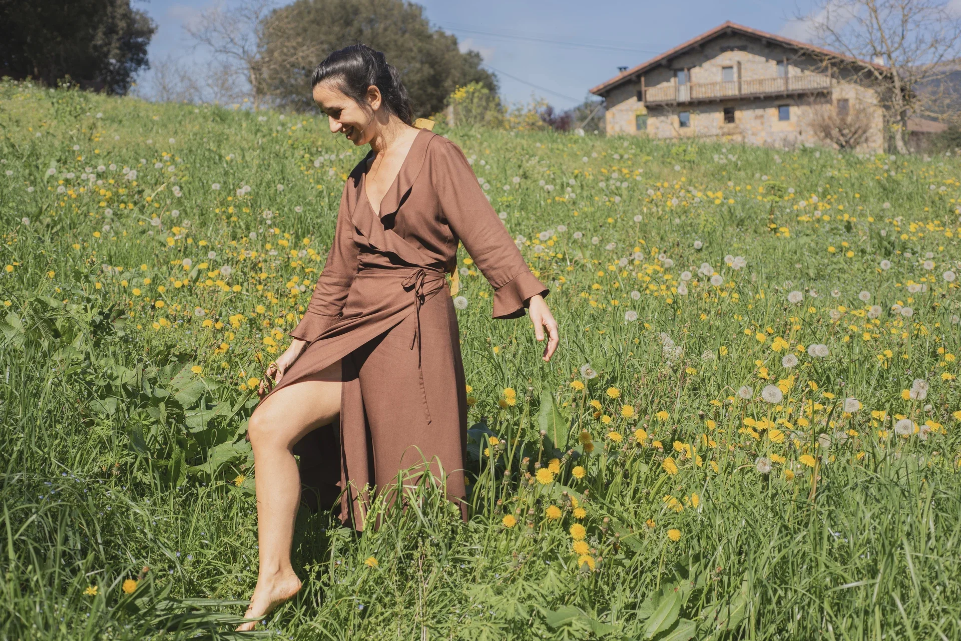 Mujer paseando por el campo vistiendo el vestido cruzado Agni en color marrón. Confeccionado en fibra de loto, alternativa vegana a la seda, y teñido con piel de granada y catechu