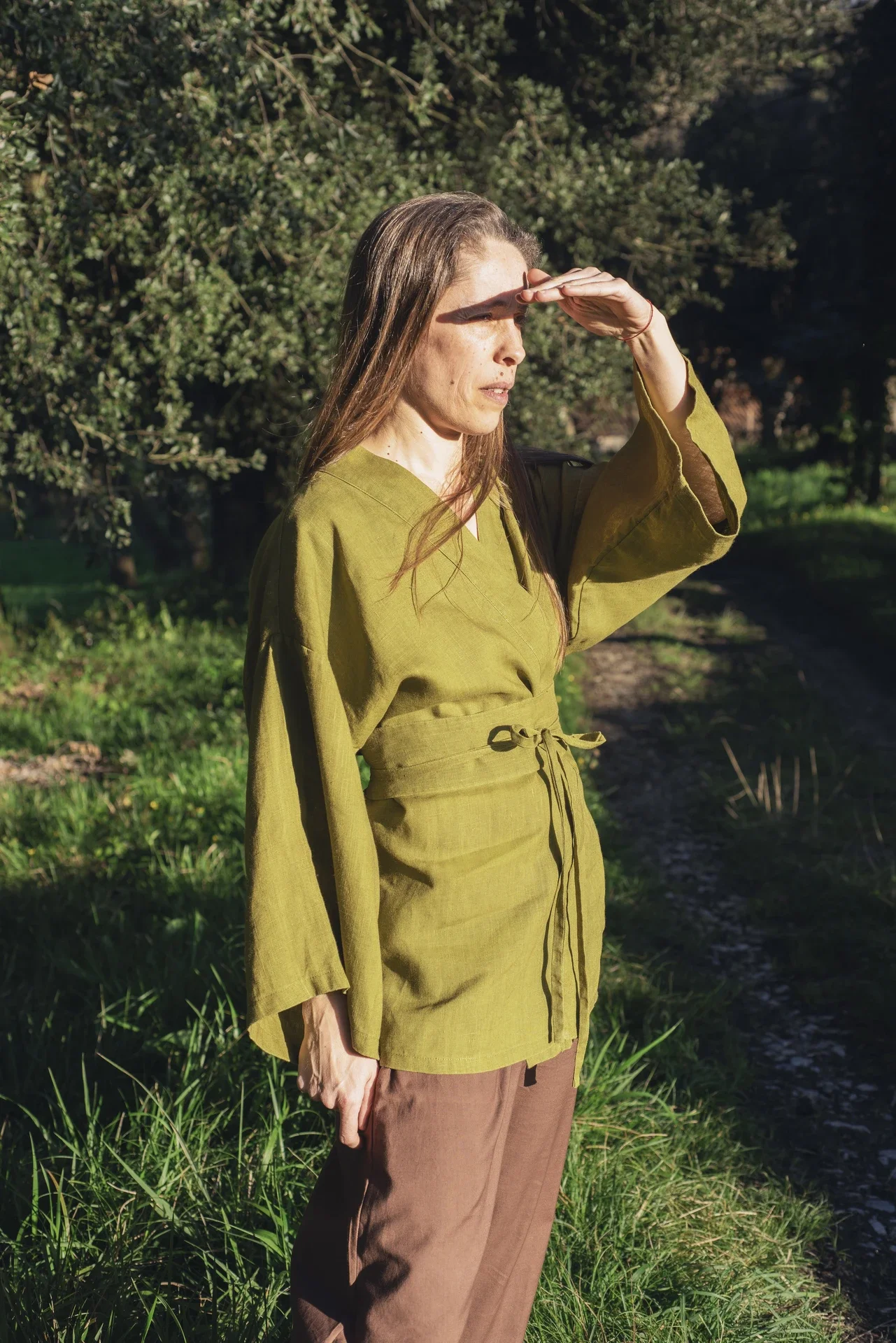 Mujer en la naturaleza vistiendo un kimono corto cruzado de lino color verde oliva, confeccionado de forma artesanal con tintes naturales libres de tóxicos.