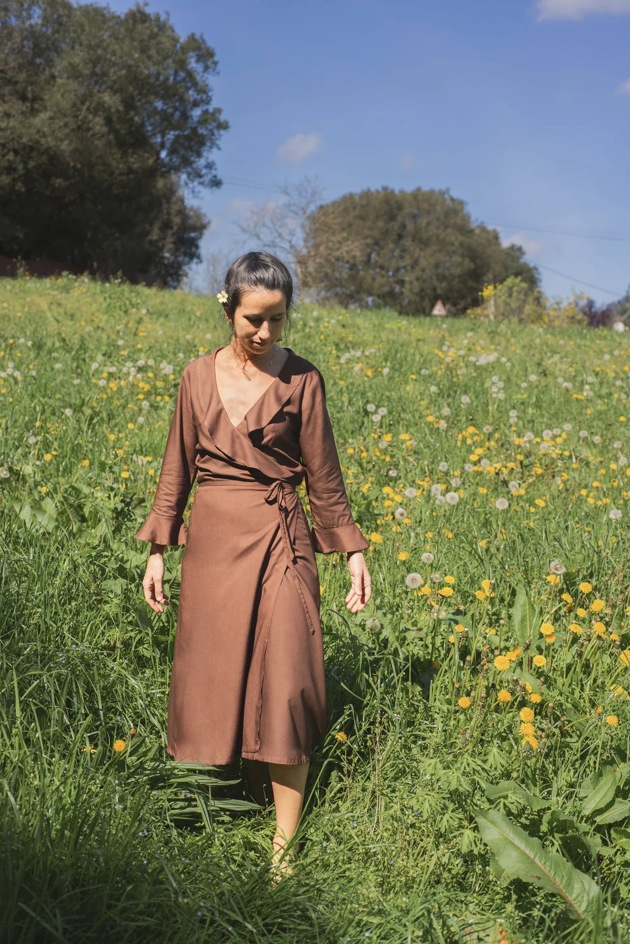 Mujer paseando por el campo vistiendo el vestido cruzado Agni en color marrón. Confeccionado en fibra de loto, alternativa vegana a la seda, y teñido con piel de granada y catechu