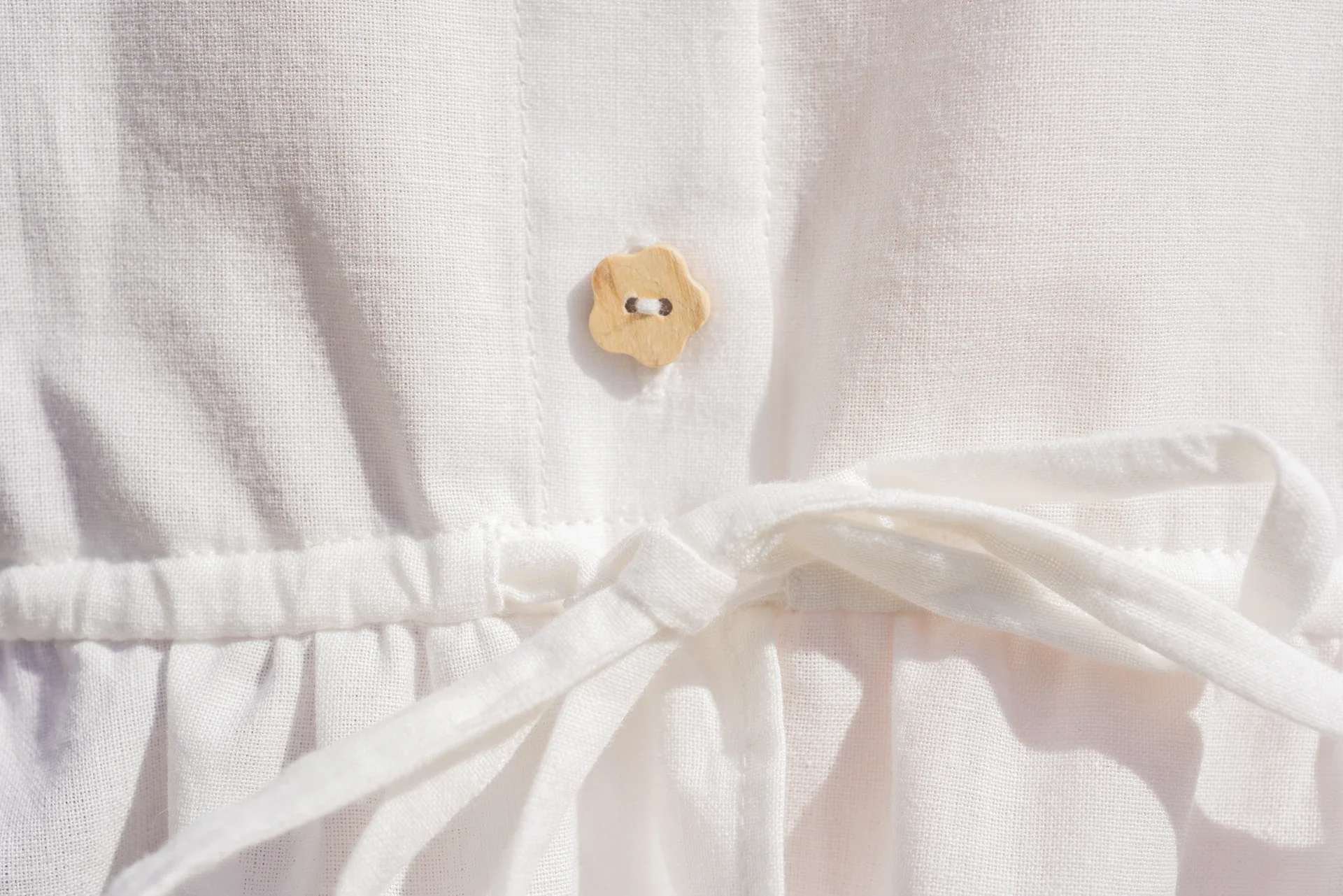 Blusa Aura de algodón orgánico en blanco, destacando sus botones de madera en forma de flor y el lazo ajustable en la cintura.