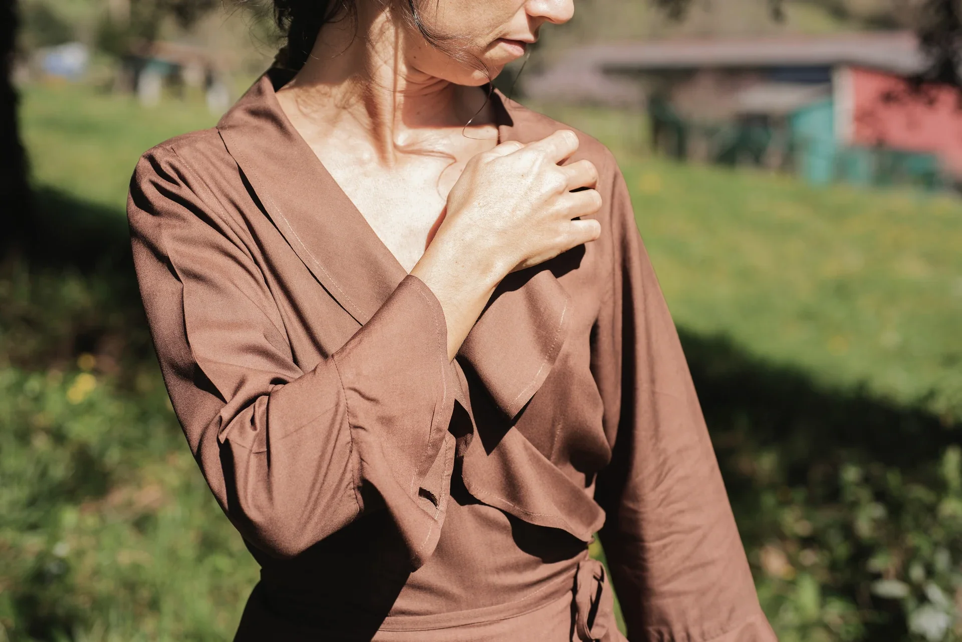 Mujer paseando por el campo vistiendo el vestido cruzado Agni en color marrón. Confeccionado en fibra de loto, alternativa vegana a la seda, y teñido con piel de granada y catechu