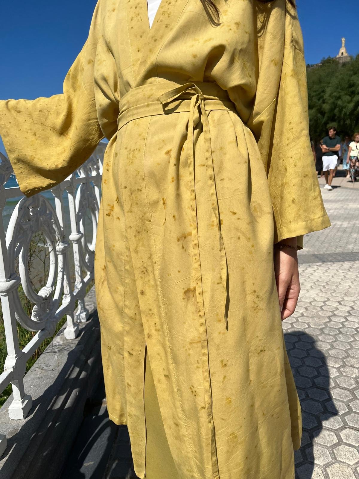 Mujer sonriendo en la naturaleza vistiendo un kimono cruzado verde oliva de fibra de loto con estampado botánico eco-print.