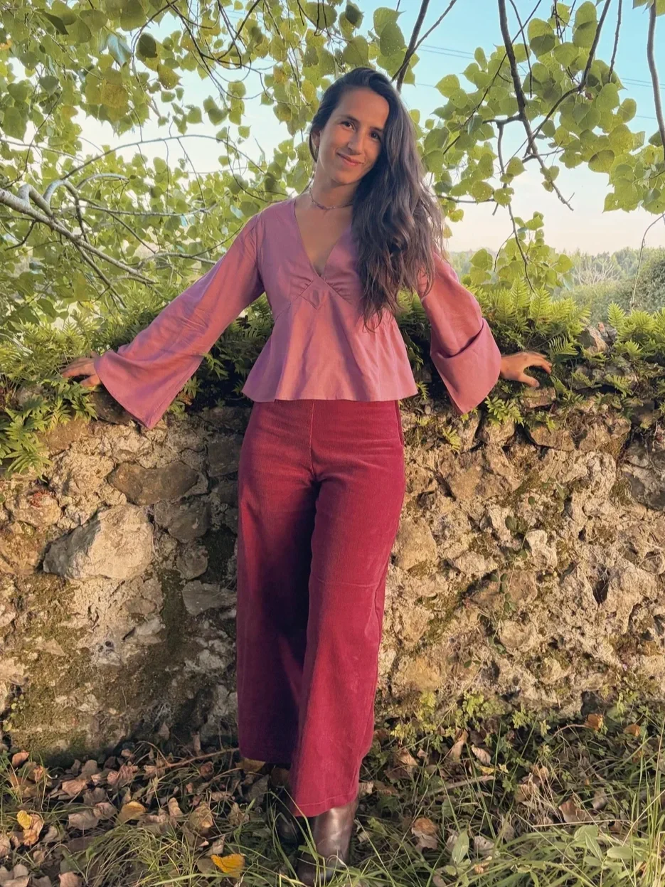 Mujer sonriente en el bosque luciendo el pantalón Indira de pana.