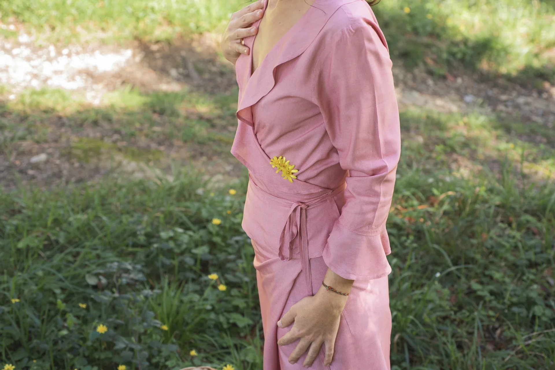 Mujer vistiendo la Blusa Agni cruzada de color rosa suave, confeccionada en fibra de loto natural con detalles de volantes en las mangas