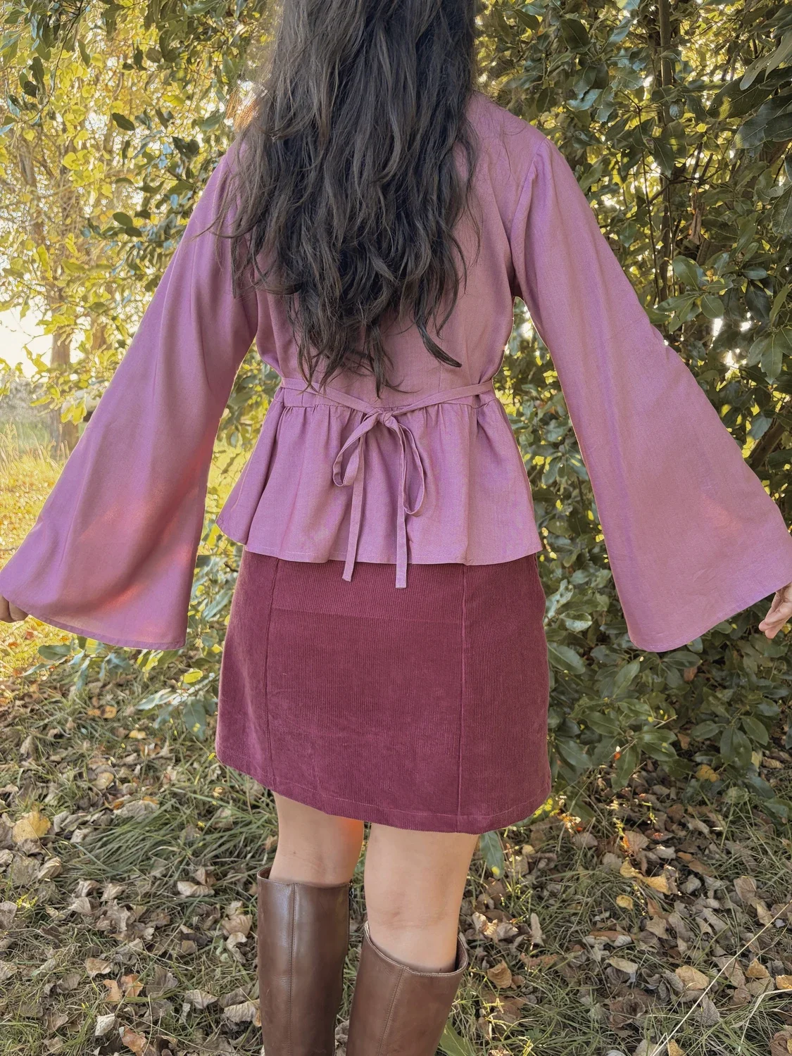 Mujer en la naturaleza luciendo la blusa mística Devi en color violeta, destacando las amplias mangas acampanadas y el tejido teñido con plantas medicinales