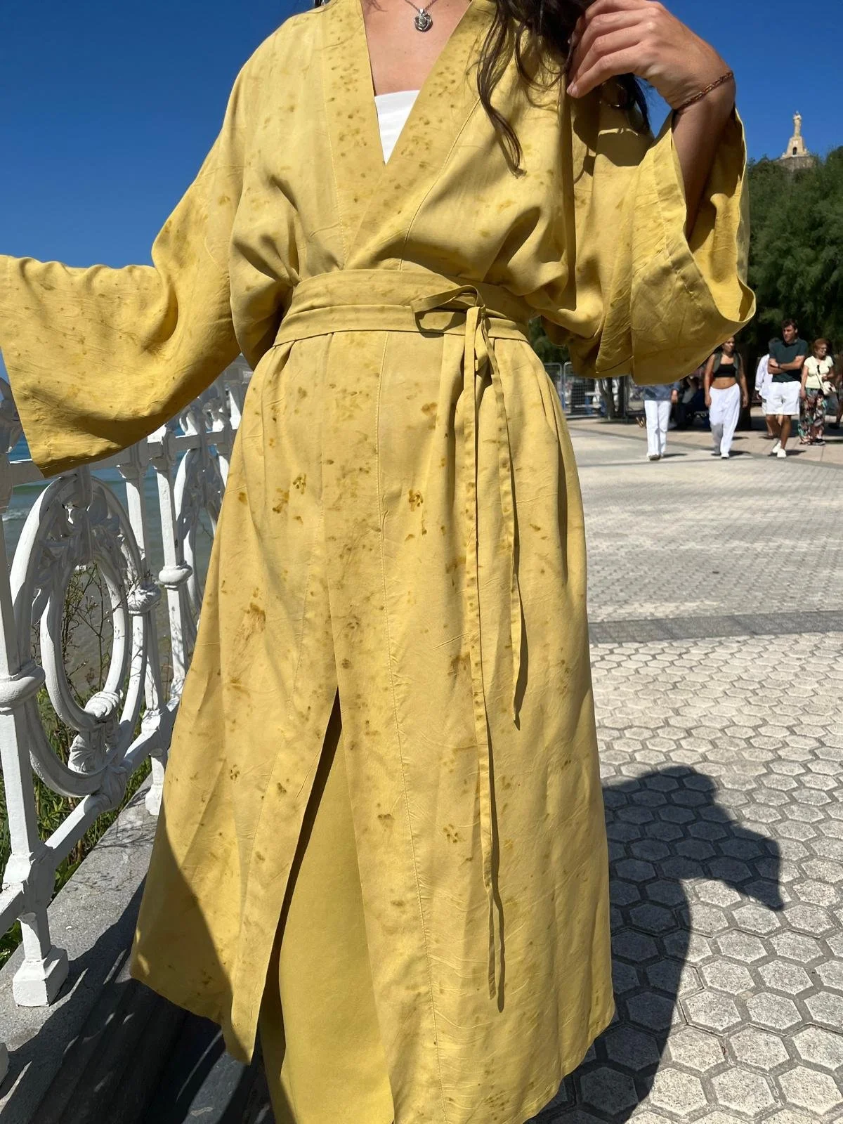 Mujer sonriendo en la naturaleza vistiendo un kimono cruzado verde oliva de fibra de loto con estampado botánico eco-print.
