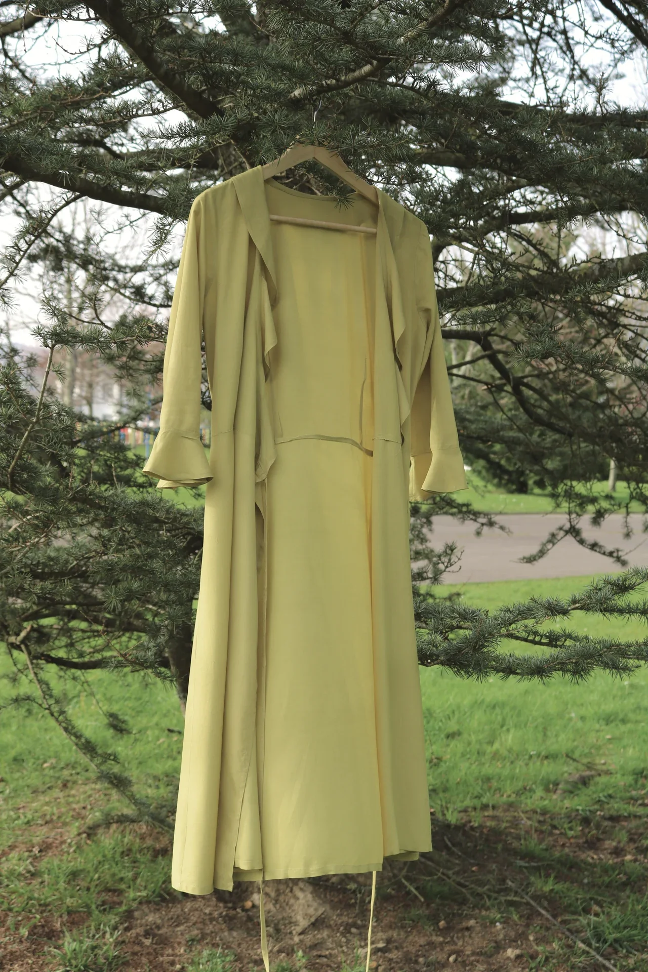 Mujer paseando por el campo vistiendo el vestido cruzado Agni en color marrón. Confeccionado en fibra de loto, alternativa vegana a la seda, y teñido con piel de granada y catechu