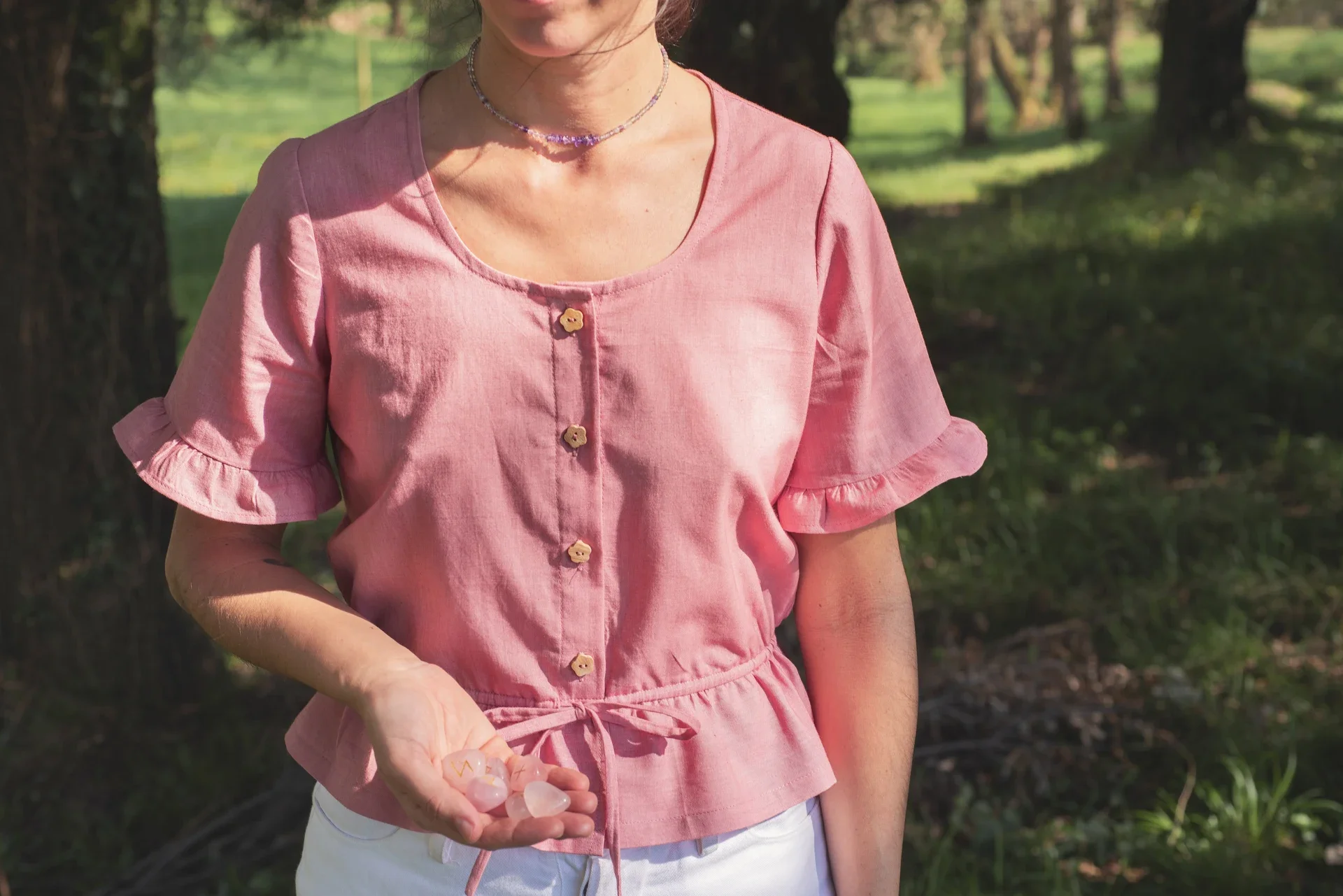Blusa Aura de algodón orgánico en rosa de Madder Root, destacando sus botones de madera en forma de flor y el lazo ajustable en la cintura.