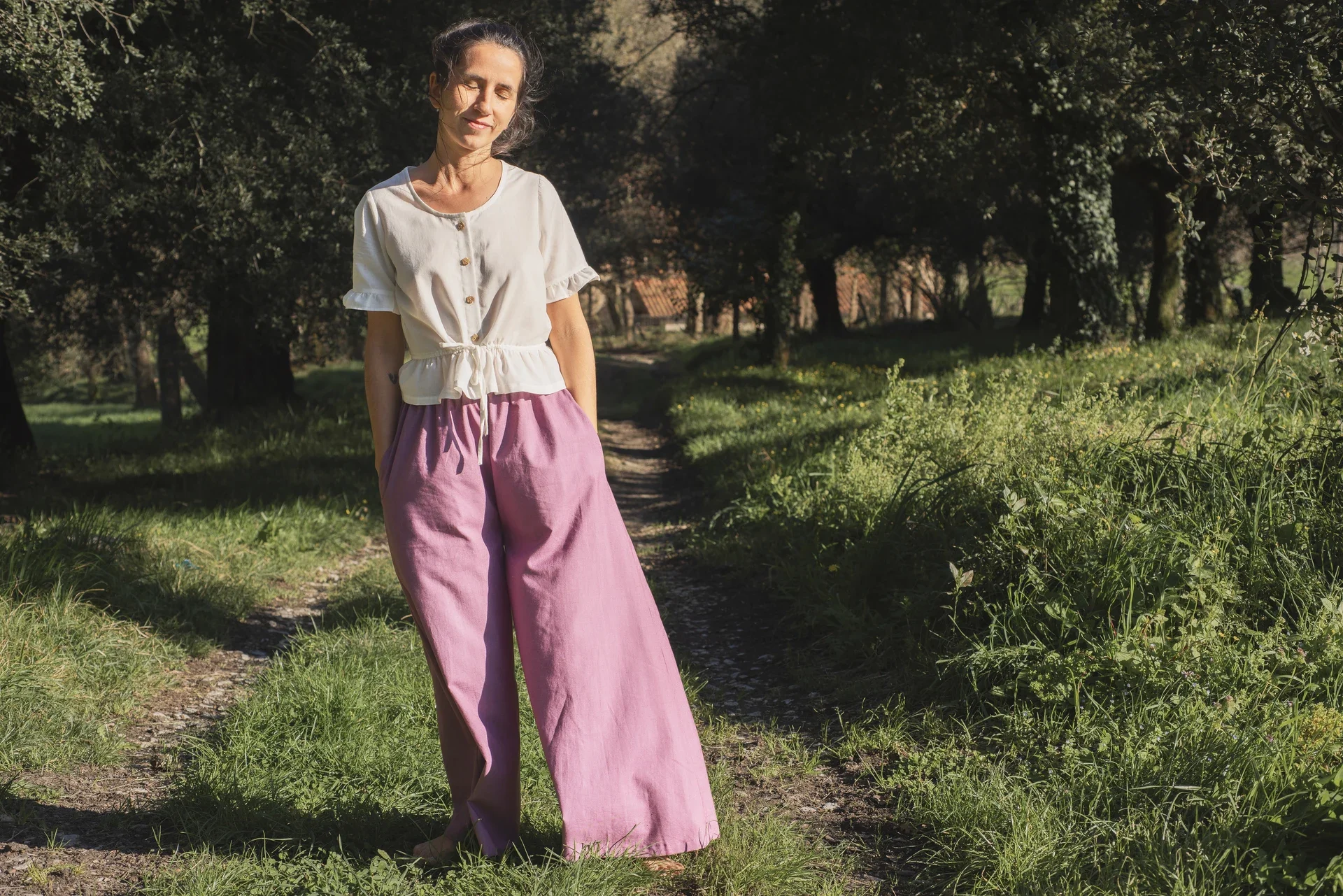 Mujer en la naturaleza vistiendo el Pantalón Orekan de pata ancha en color blanco, confeccionado en algodón orgánico y tintes naturales libres de tóxicos