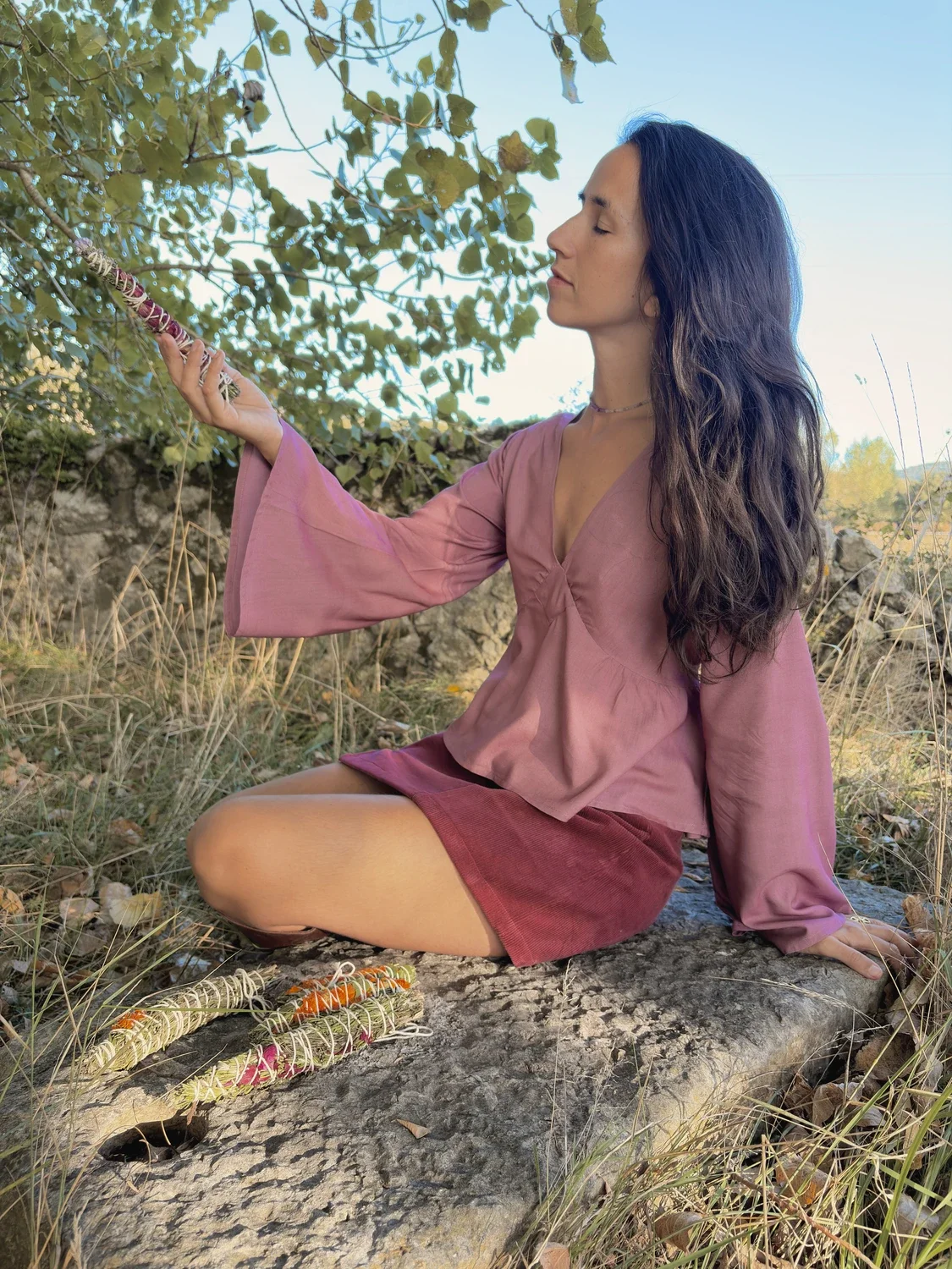 Mujer en la naturaleza luciendo la blusa mística Devi en color violeta, destacando las amplias mangas acampanadas y el tejido teñido con plantas medicinales