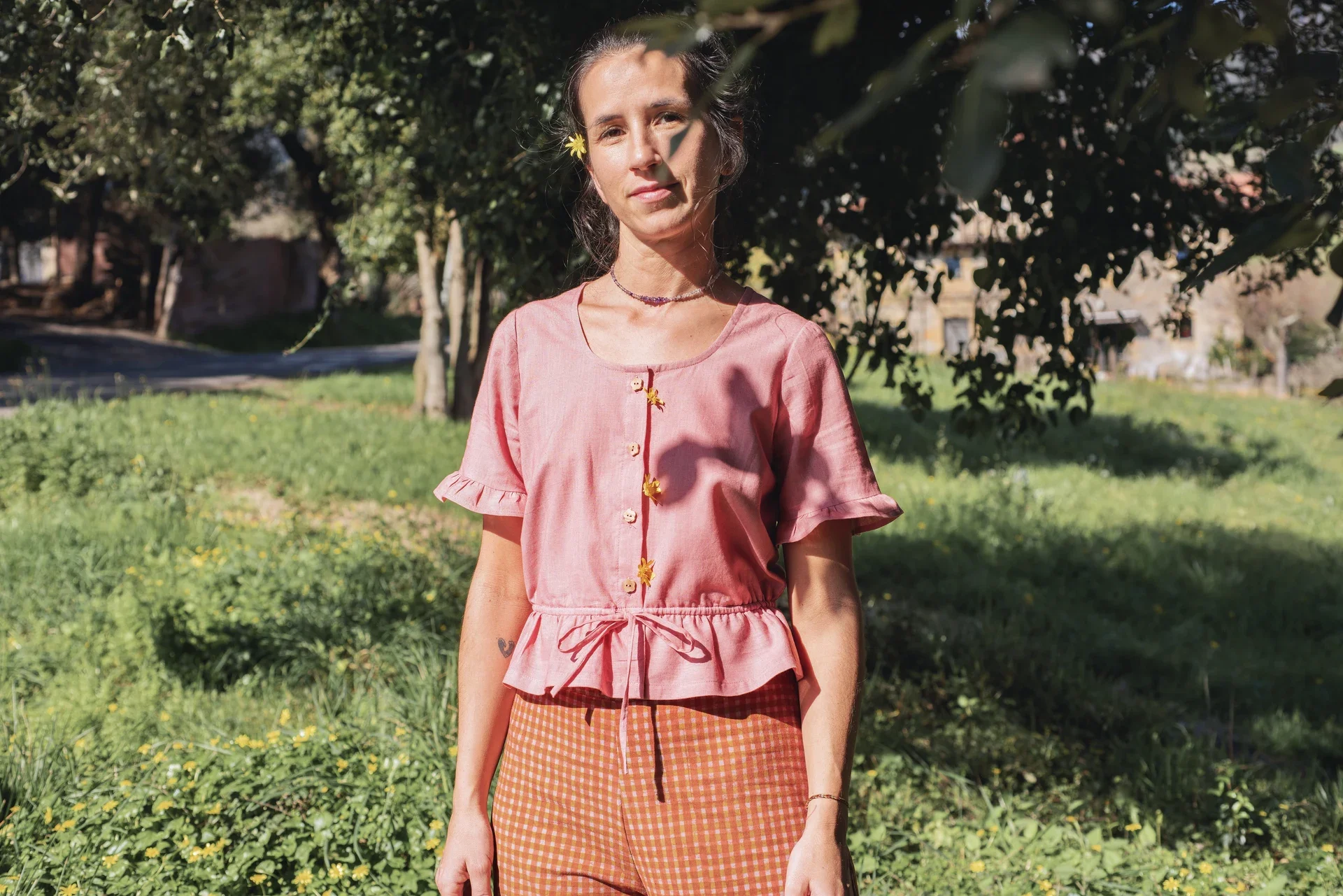 Blusa Aura de algodón orgánico en rosa de Madder Root, destacando sus botones de madera en forma de flor y el lazo ajustable en la cintura.