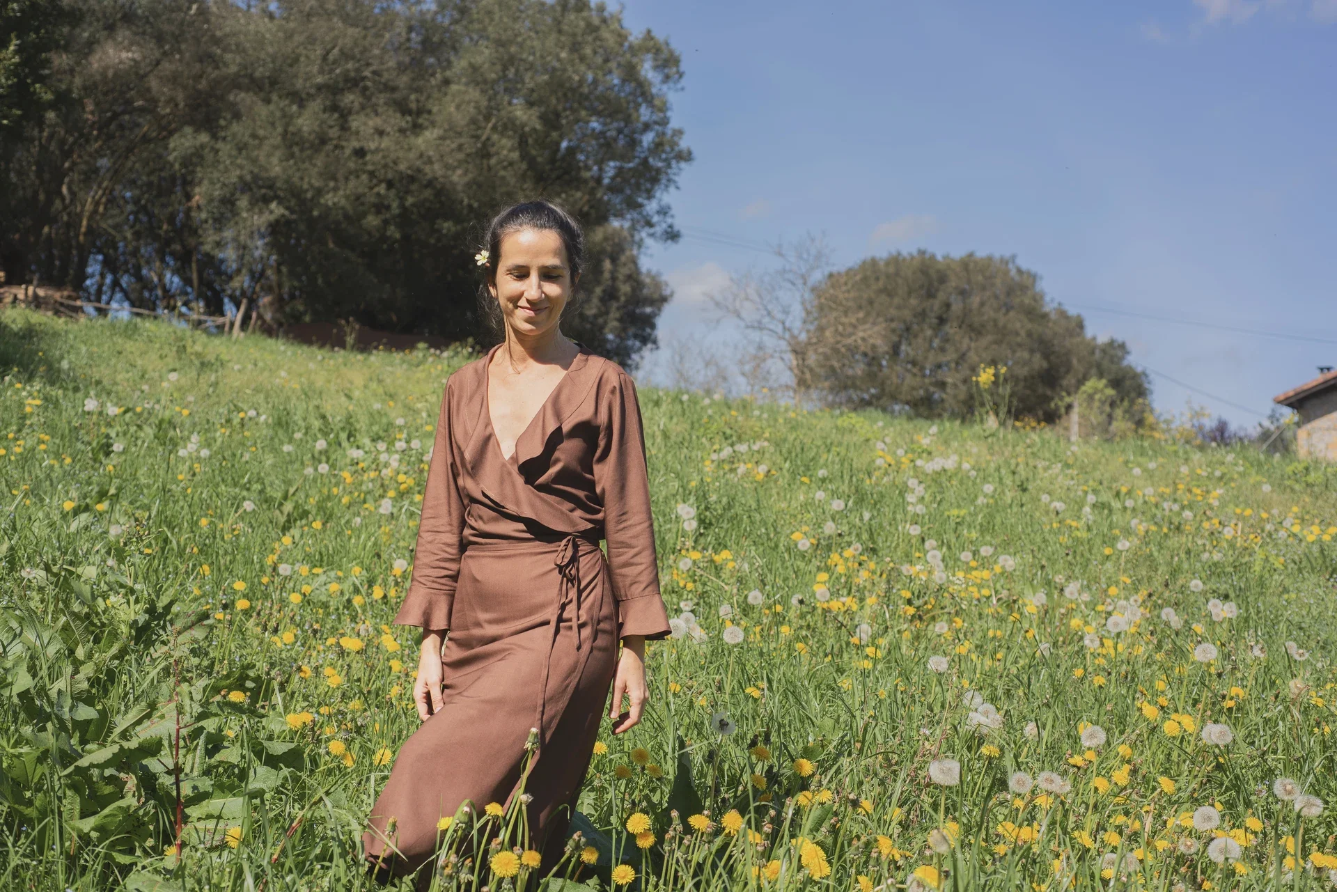 Mujer paseando por el campo vistiendo el vestido cruzado Agni en color marrón. Confeccionado en fibra de loto, alternativa vegana a la seda, y teñido con piel de granada y catechu
