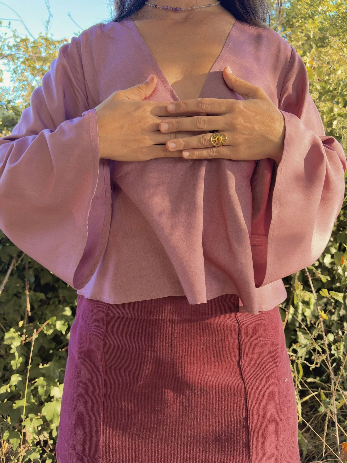 Mujer en la naturaleza luciendo la blusa mística Devi en color violeta, destacando las amplias mangas acampanadas y el tejido teñido con plantas medicinales