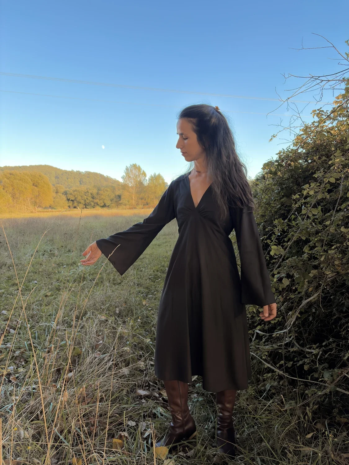 Modelo posando en un entorno natural con el vestido amuleto Devi en color negro, mostrando el vuelo de la prenda y las mangas acampanadas de estilo brujita