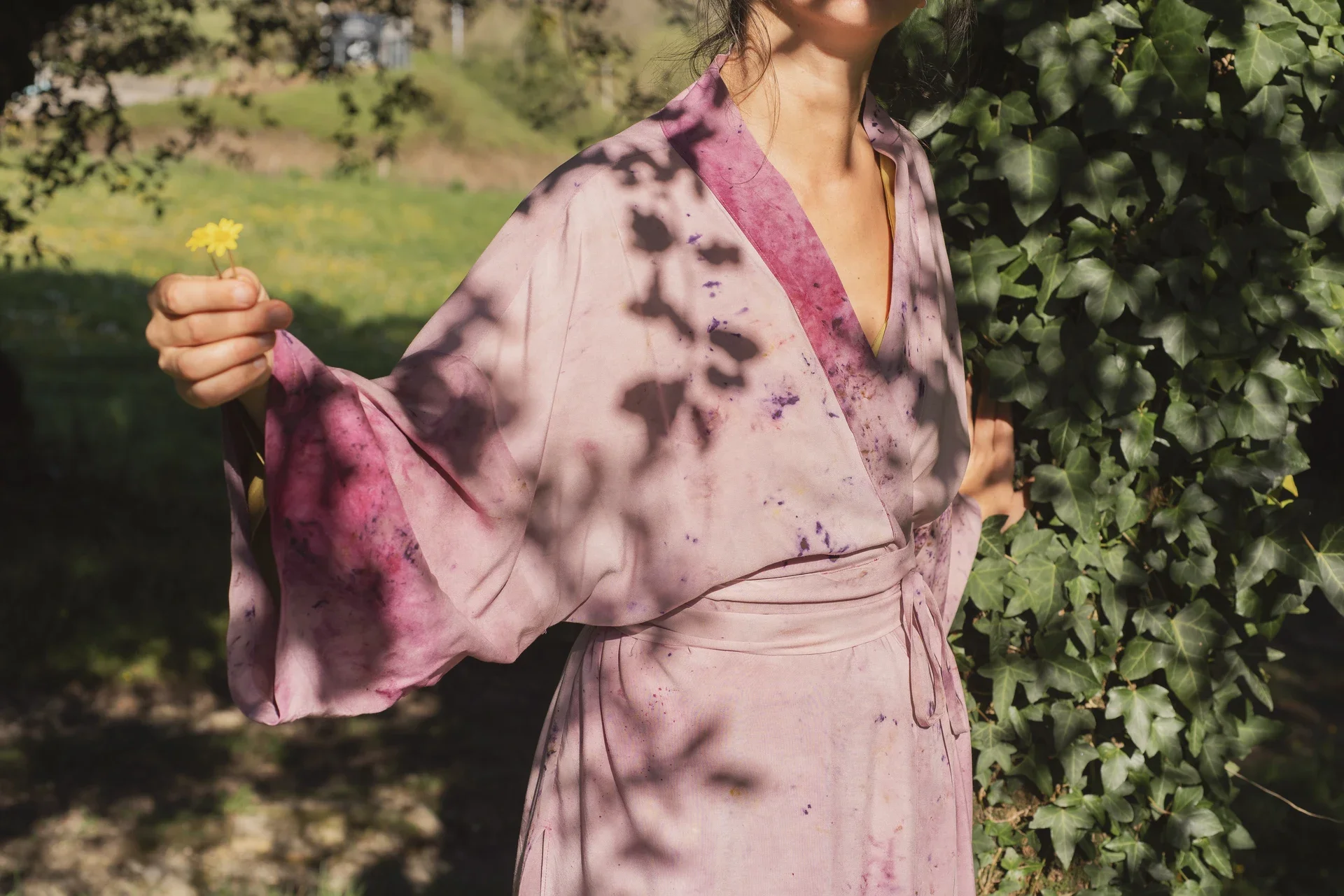 Mujer meditando al aire libre, vistiendo un kimono fluido color morado de fibra de loto con estampado botánico eco-print.
