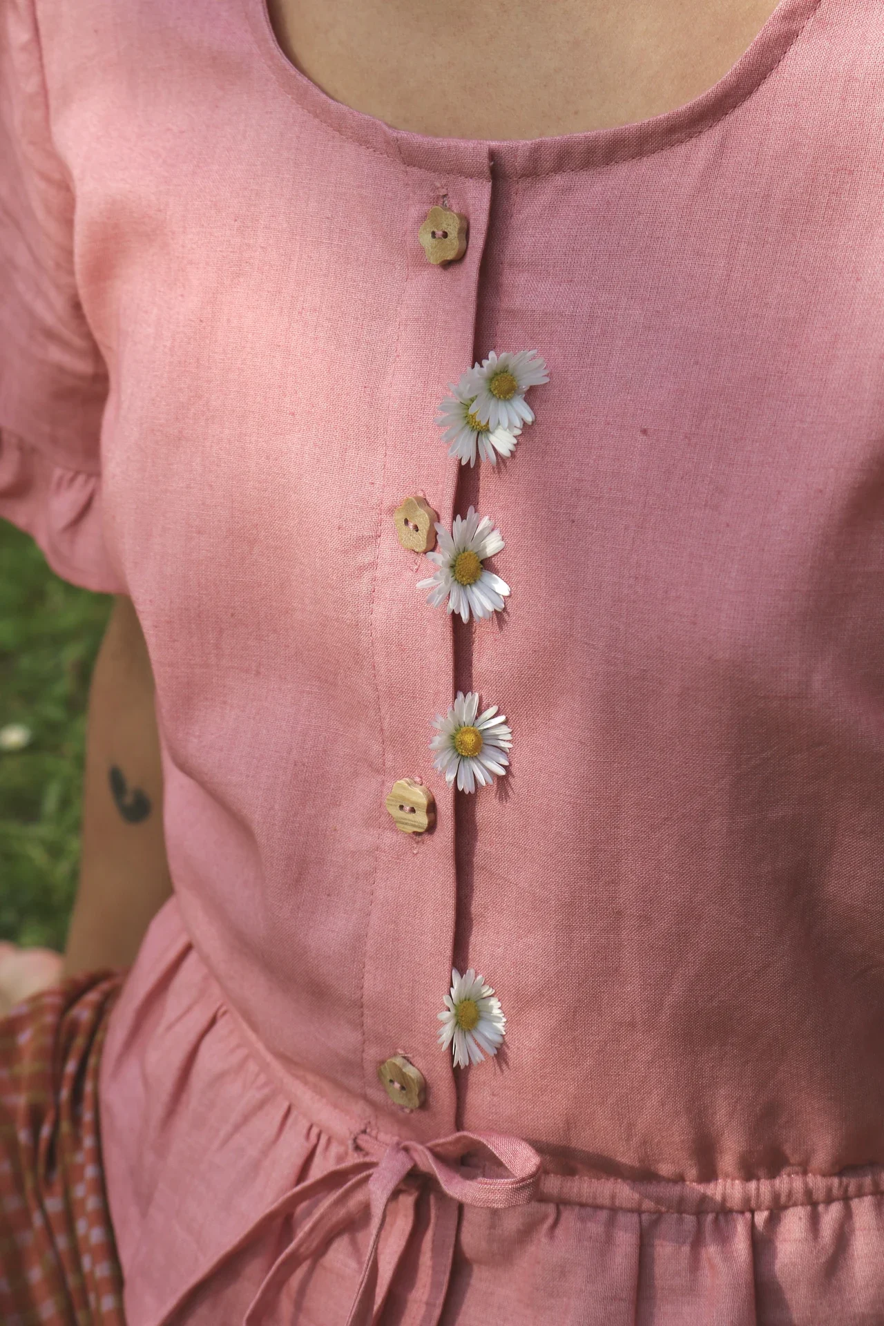 Blusa Aura de algodón orgánico en rosa de Madder Root, destacando sus botones de madera en forma de flor y el lazo ajustable en la cintura.