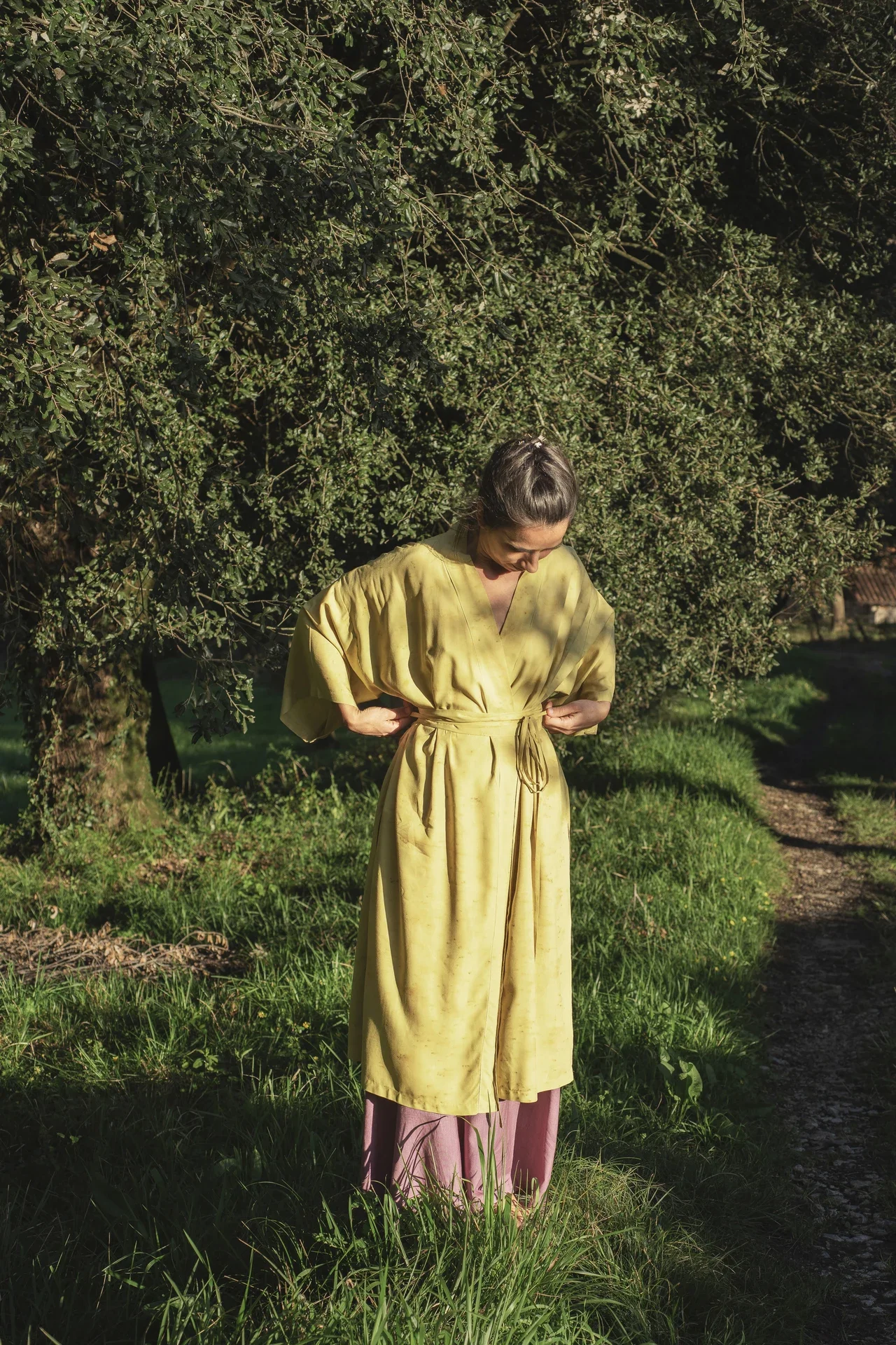 Mujer sonriendo en la naturaleza vistiendo un kimono cruzado verde oliva de fibra de loto con estampado botánico eco-print.