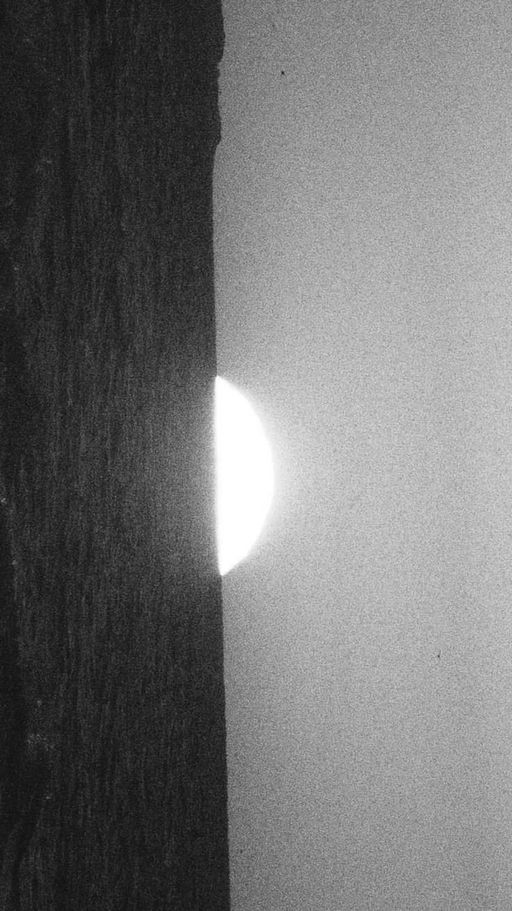 Sunset or sunrise over the ocean with the sun partially hidden behind a dark silhouette of land or a beach.