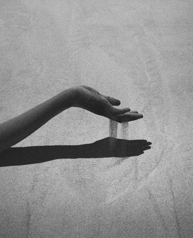 Black and white photo of a person's hand with fingers slightly curved, casting a shadow on a textured wall, creating a visual illusion of a floating hand.