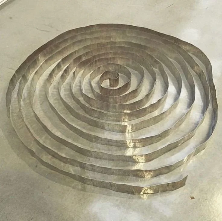 Spiral-shaped metallic sculpture on a concrete floor.