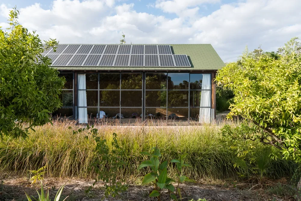 A house with outdoor solar panels on its roof, surrounded by trees and grass.