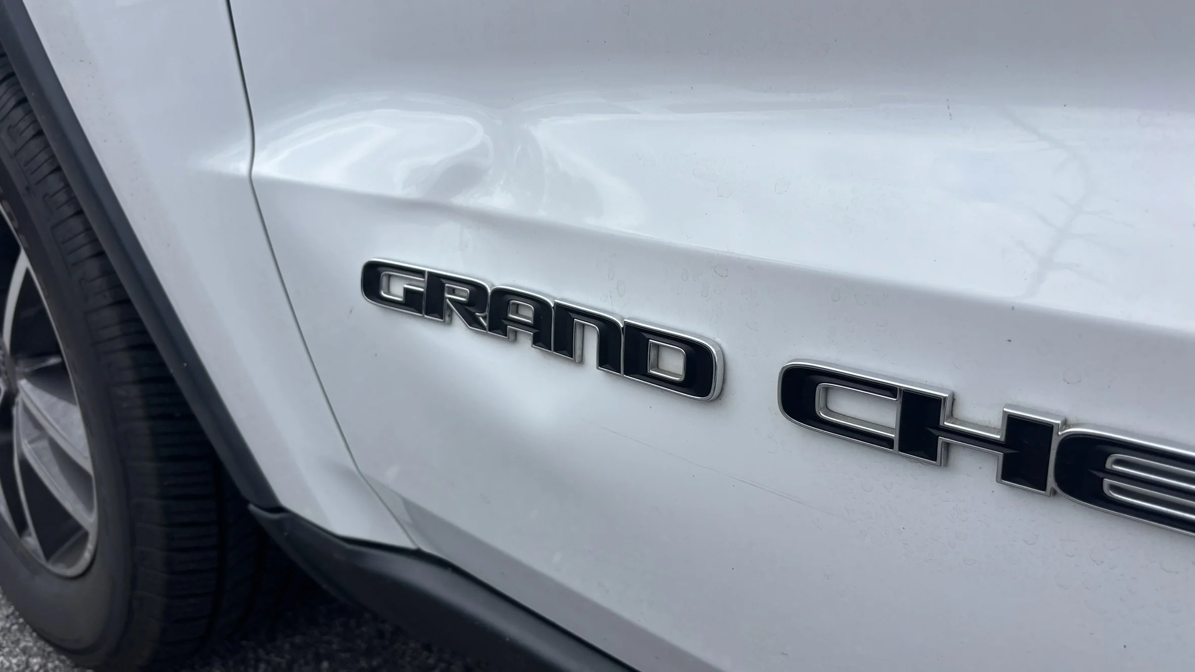 Close-up of a white Chevrolet Grand Chervolet badge on the side of a car, with a wheel partially visible on the left.