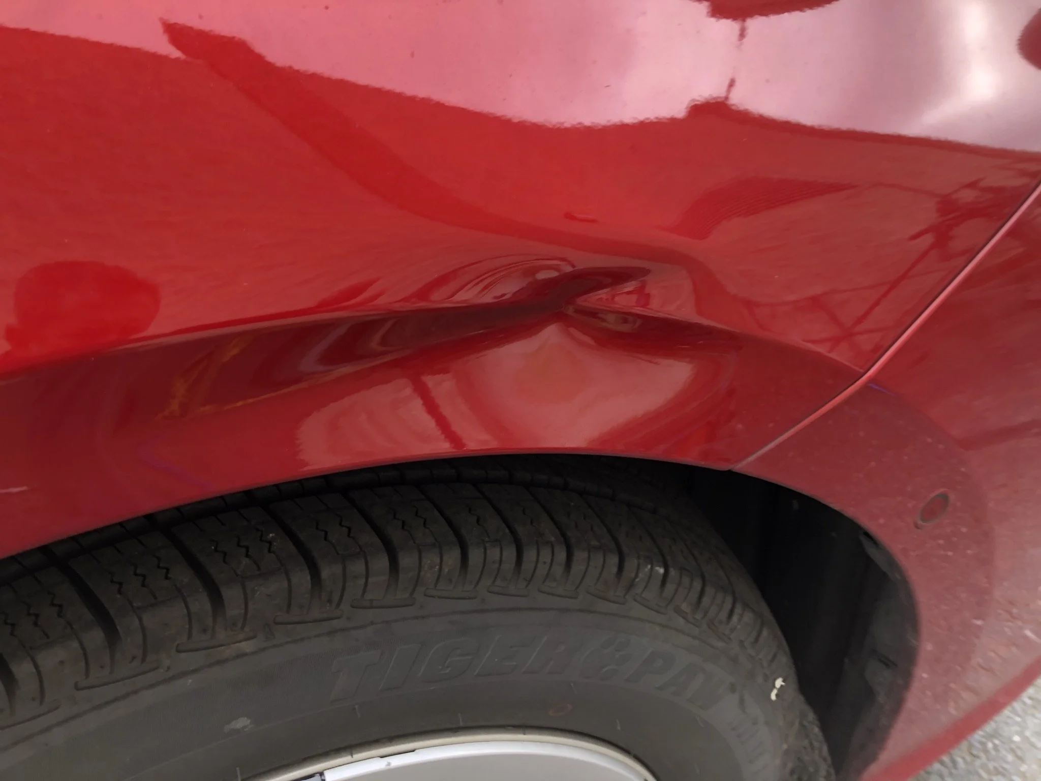 Close-up of a red car with a dent above the wheel arch.