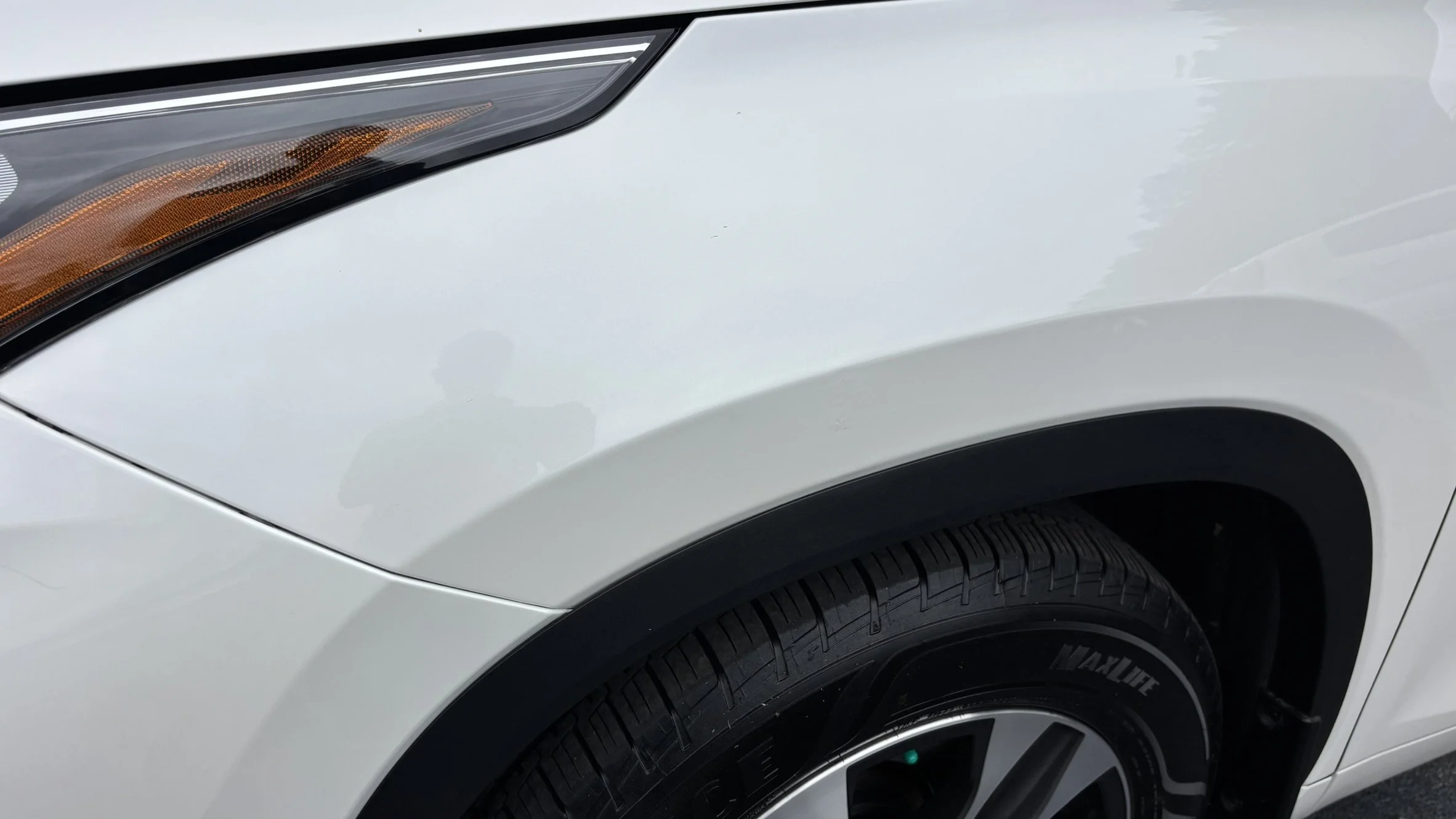 Close-up of the front right side of a white vehicle, showing the headlight, tire, and wheel well.