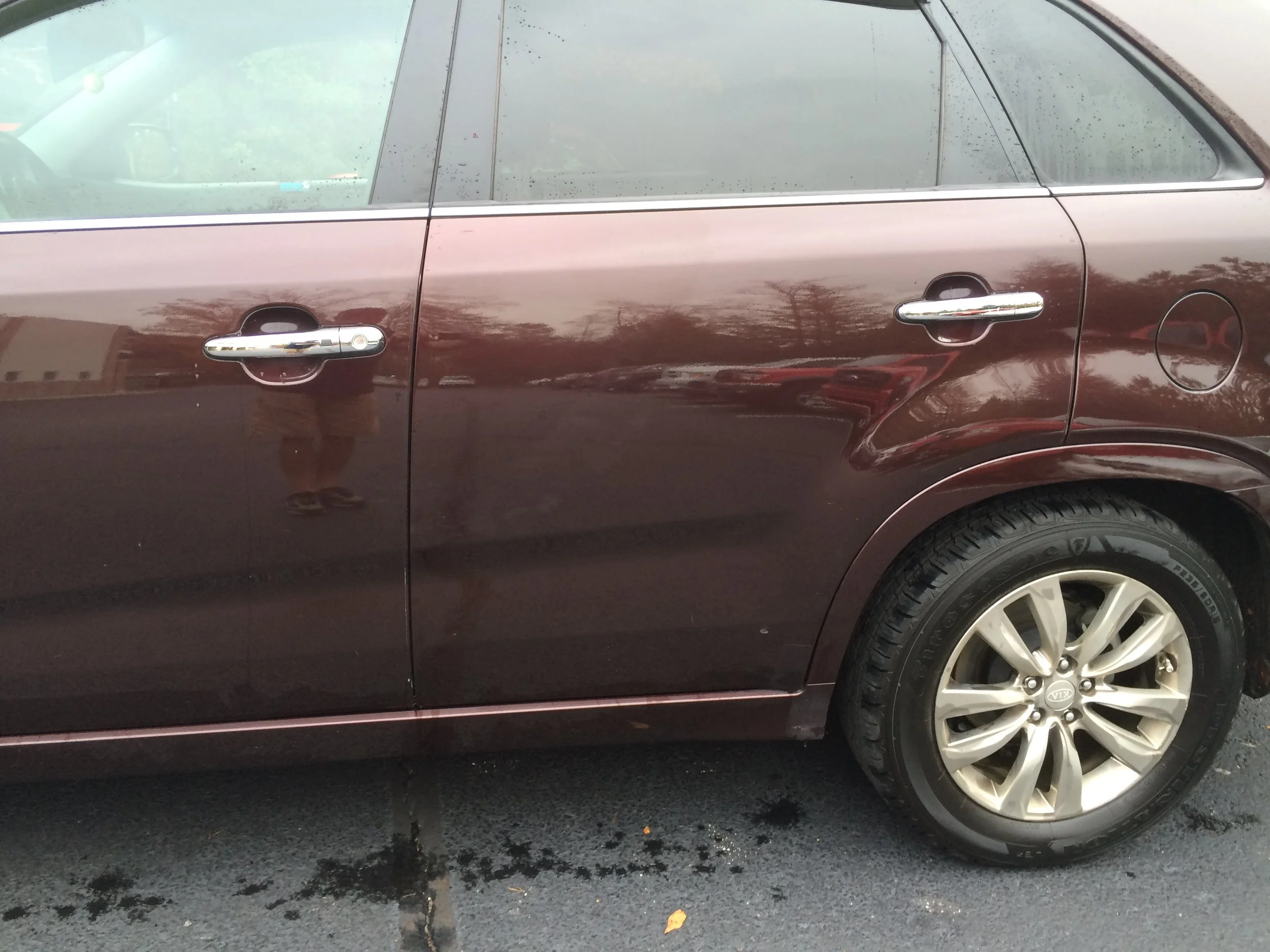 Close-up of a brown car door, handle, and wheel with tire marks on wet asphalt ground.