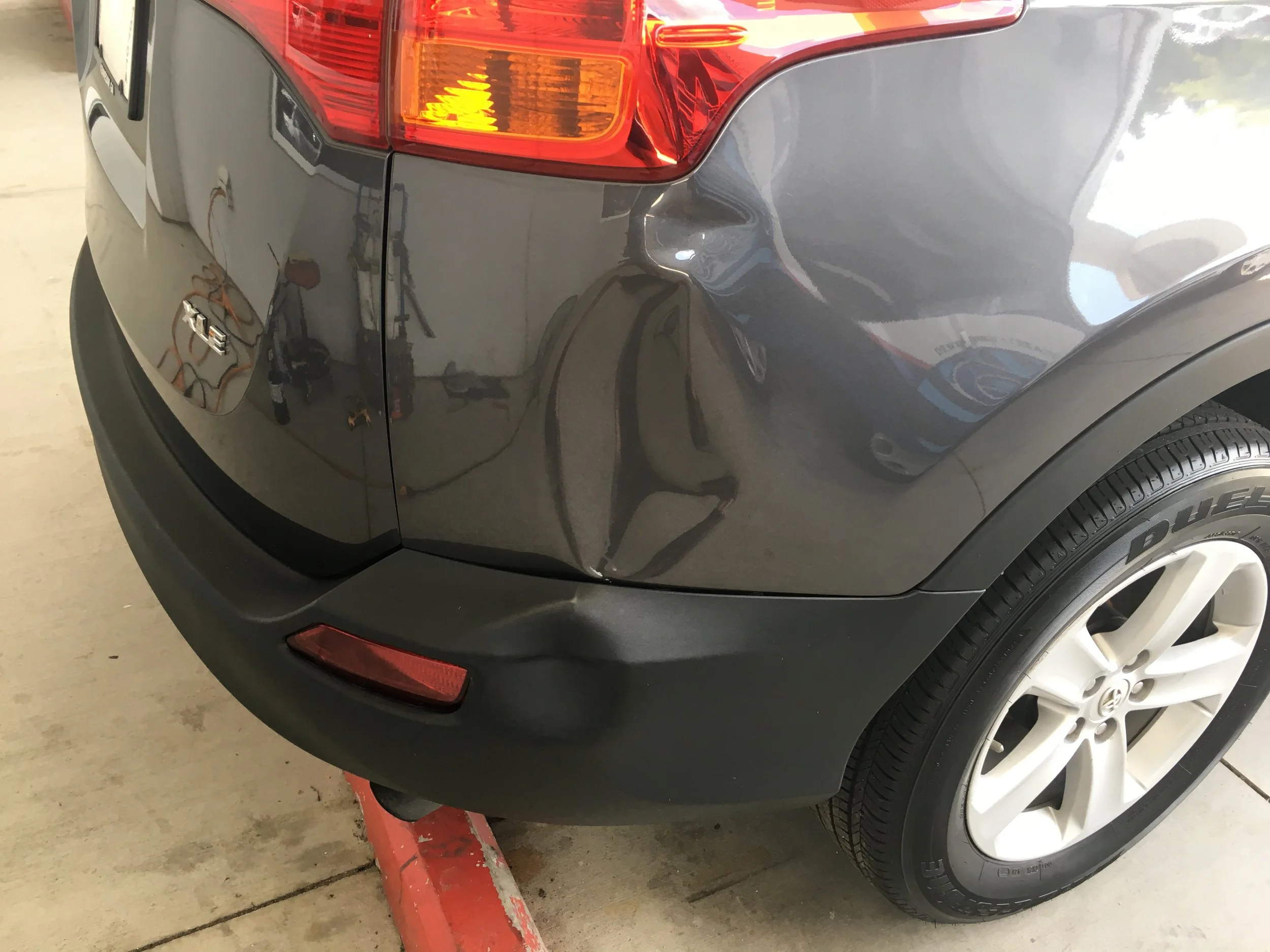 Close-up of the rear corner of a gray Volkswagen SUV, showing the tail light, tire, and part of the bumper, with reflections on the vehicle's surface.