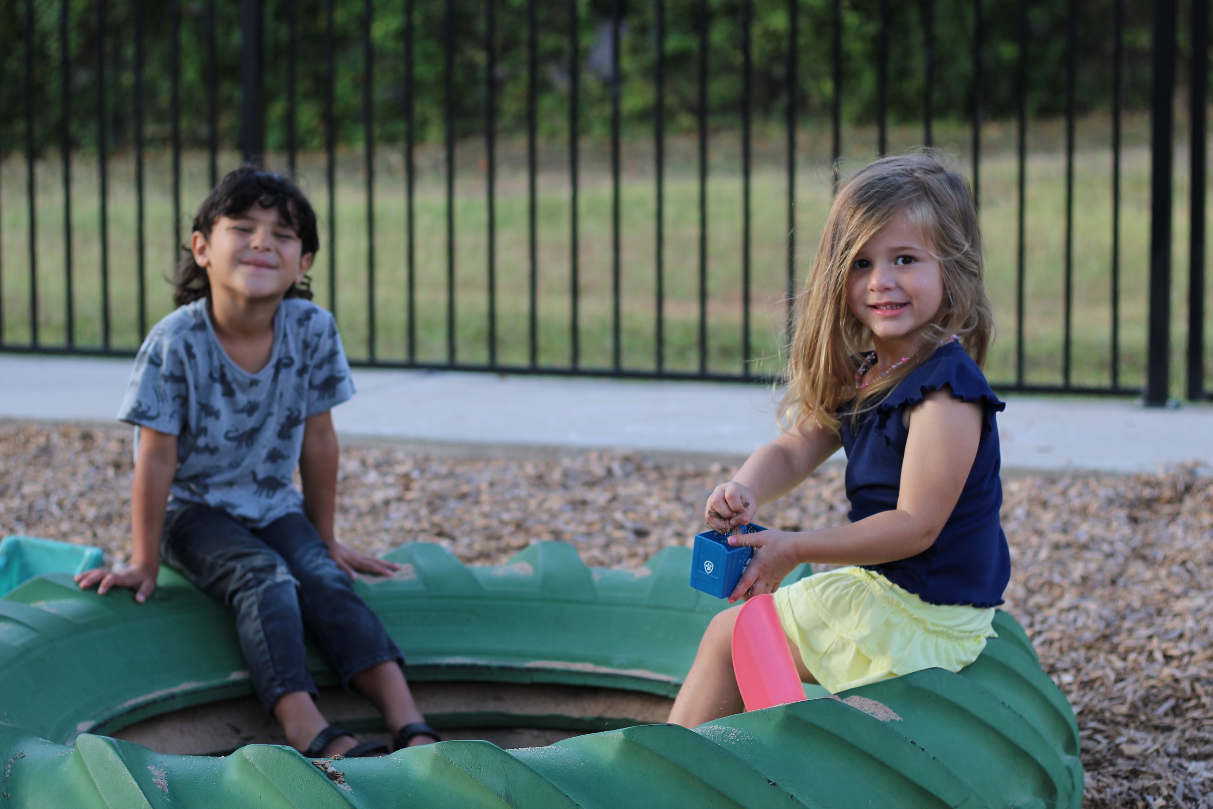 Two children, a boy and a girl, playing in a sandbox outdoors.