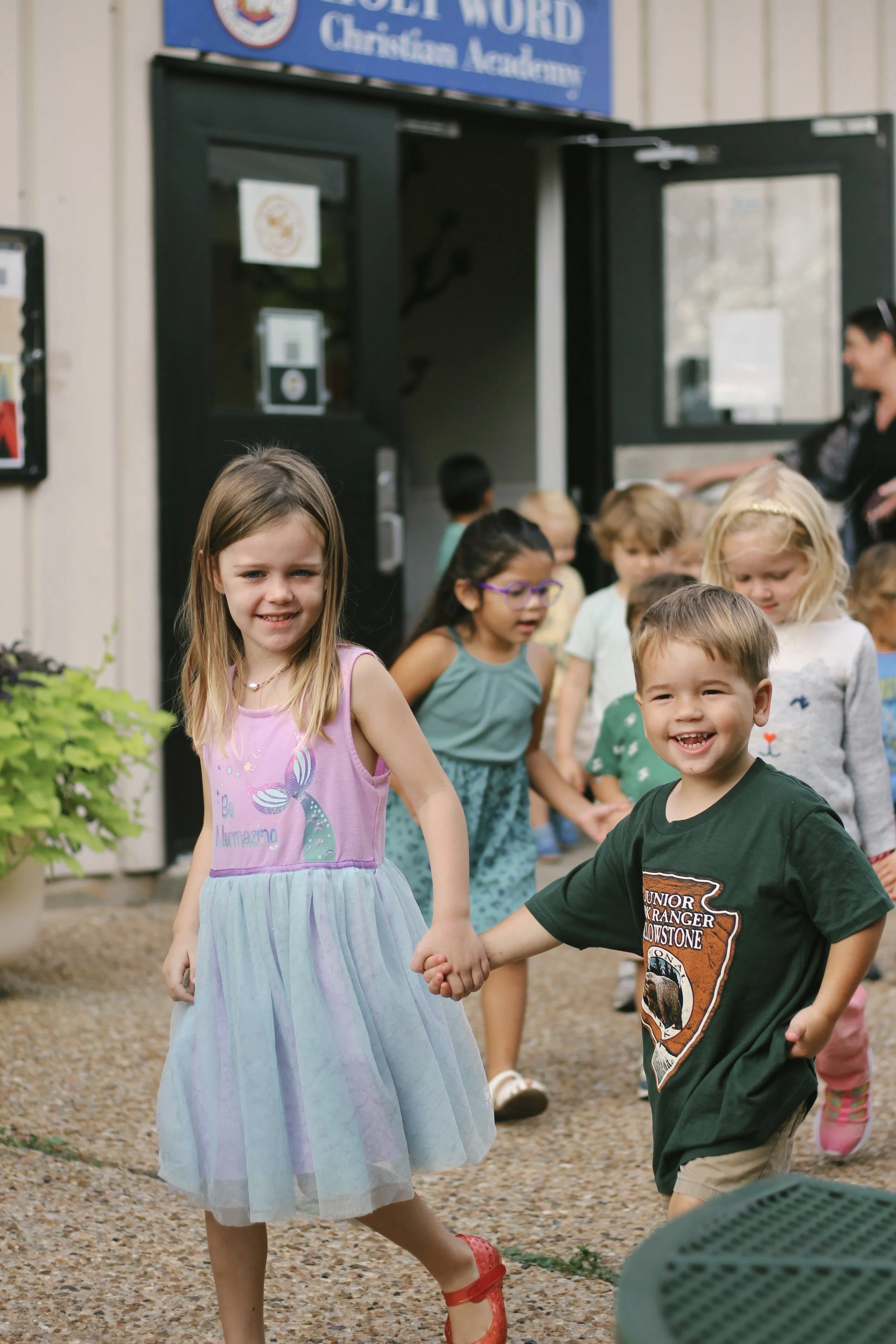 Children holding hands and walking out of a church building, smiling and enjoying themselves.