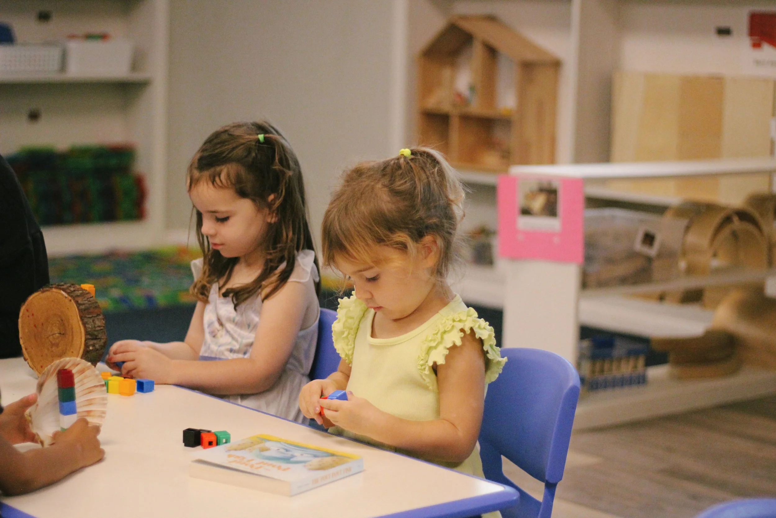 Two young girls sitting at a table, playing with colorful building blocks.