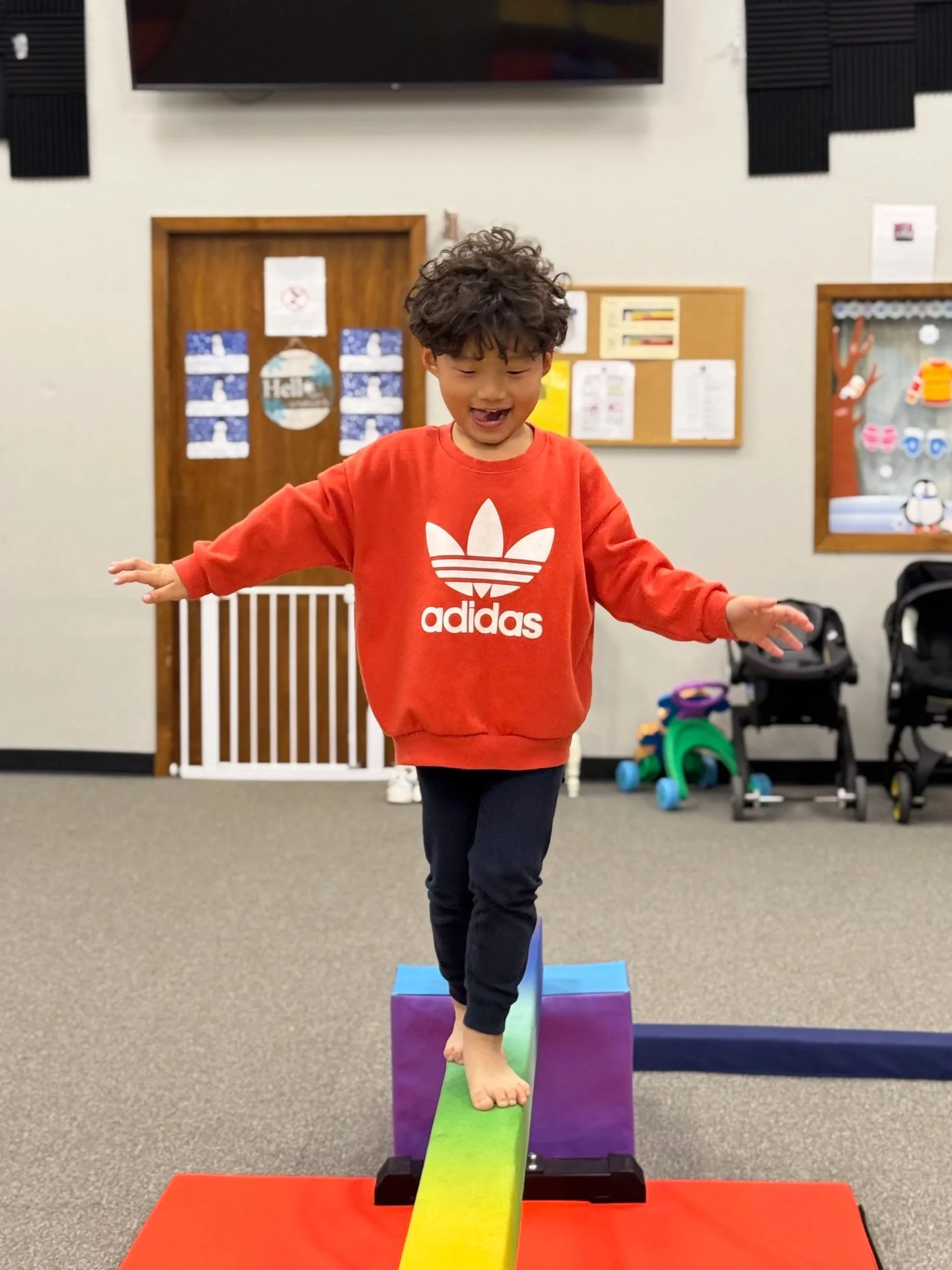 Child balancing on a colorful foam balance beam in an indoor playroom.
