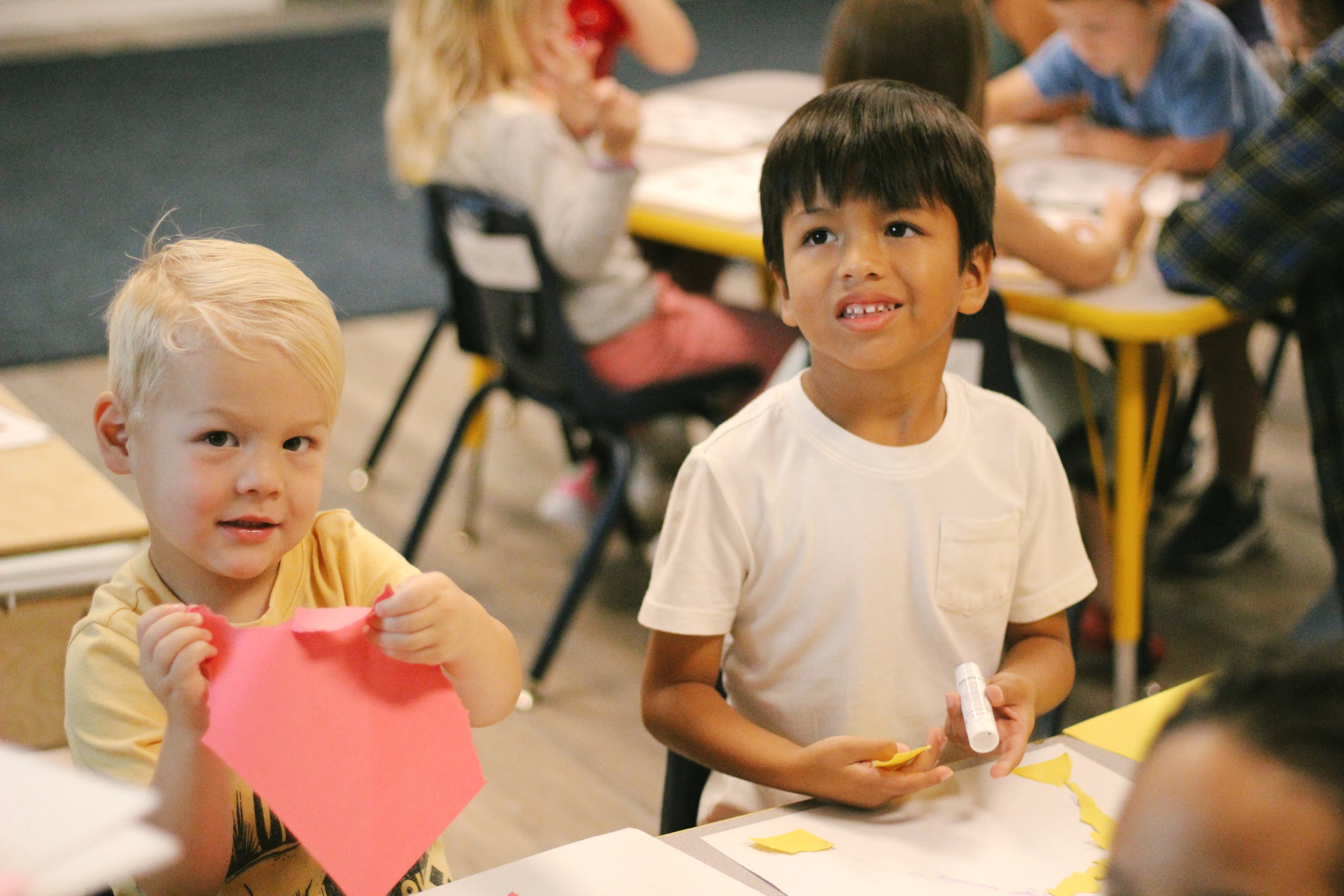 Children in a classroom participating in a craft activity, tearing and holding colored paper.
