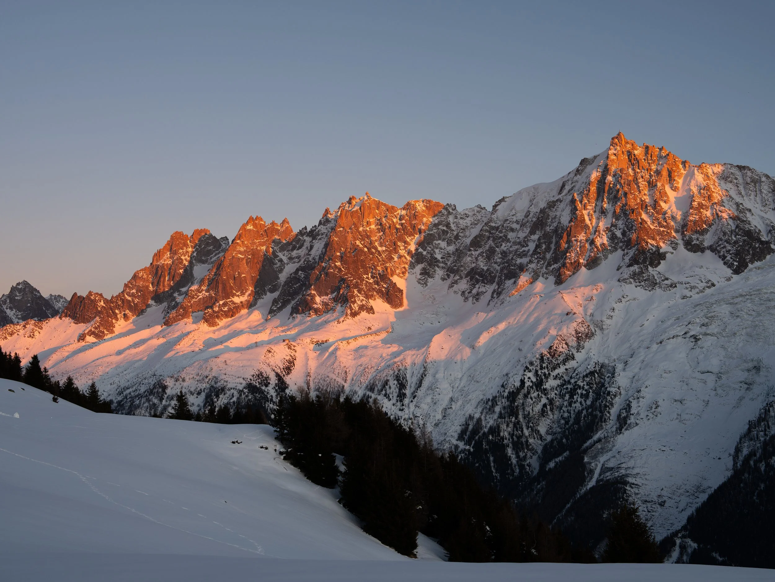 Snow-covered mountain range during sunset with a clear sky.