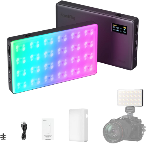 A SmallRig LED video light panel with a colorful, illuminated front and a black control unit with a display and buttons, accompanied by various accessories including a power cable, a white diffuser, a small mounting screw, a user manual, a white battery pack, and a camera with a lens.