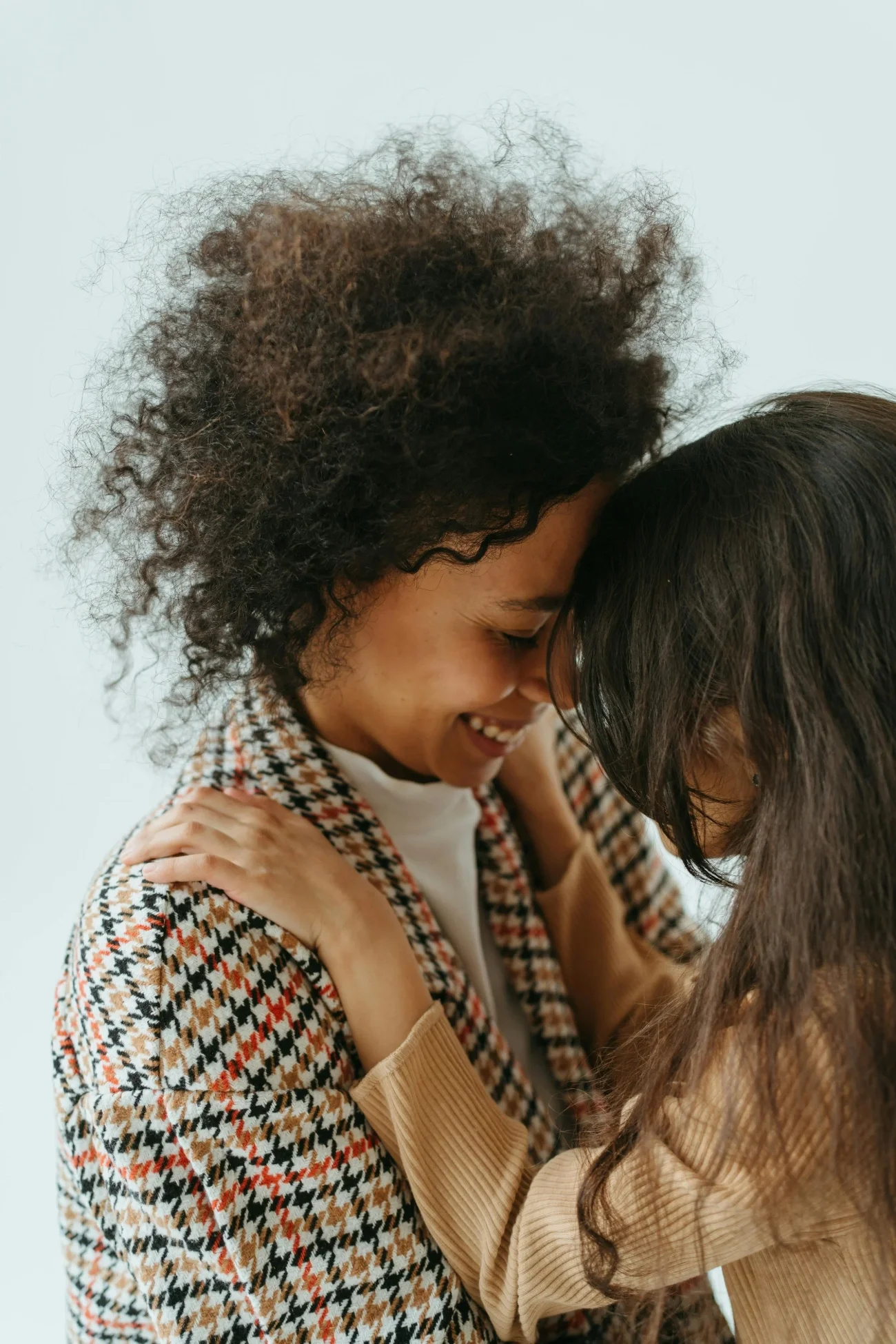 Two women embracing, their foreheads touching, sharing a joyful moment, both smiling.