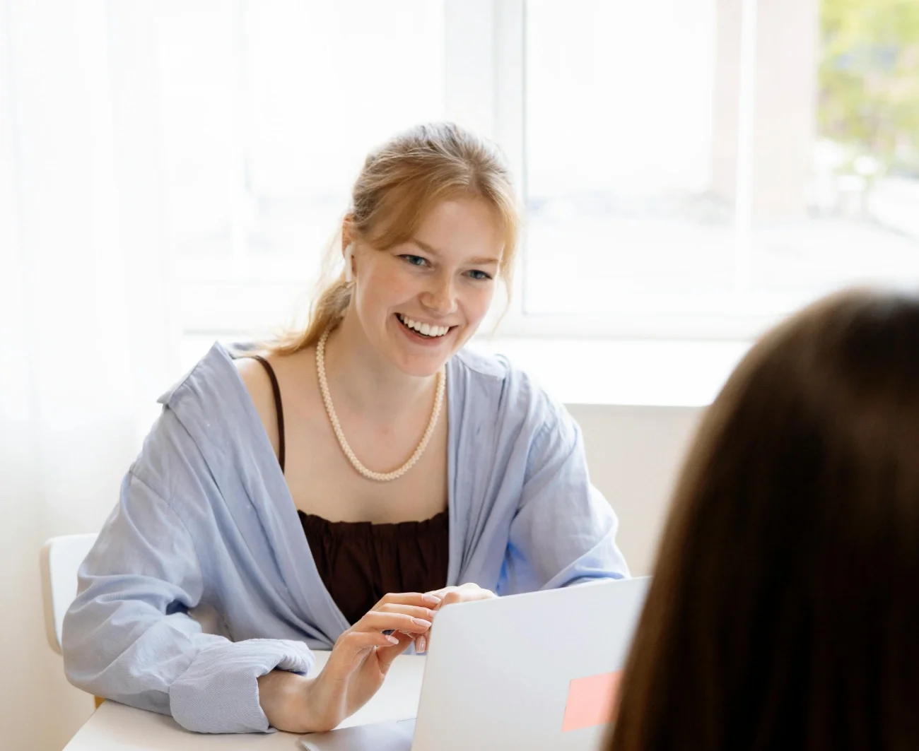A woman with red hair smiling during a conversation with another person in an office setting.