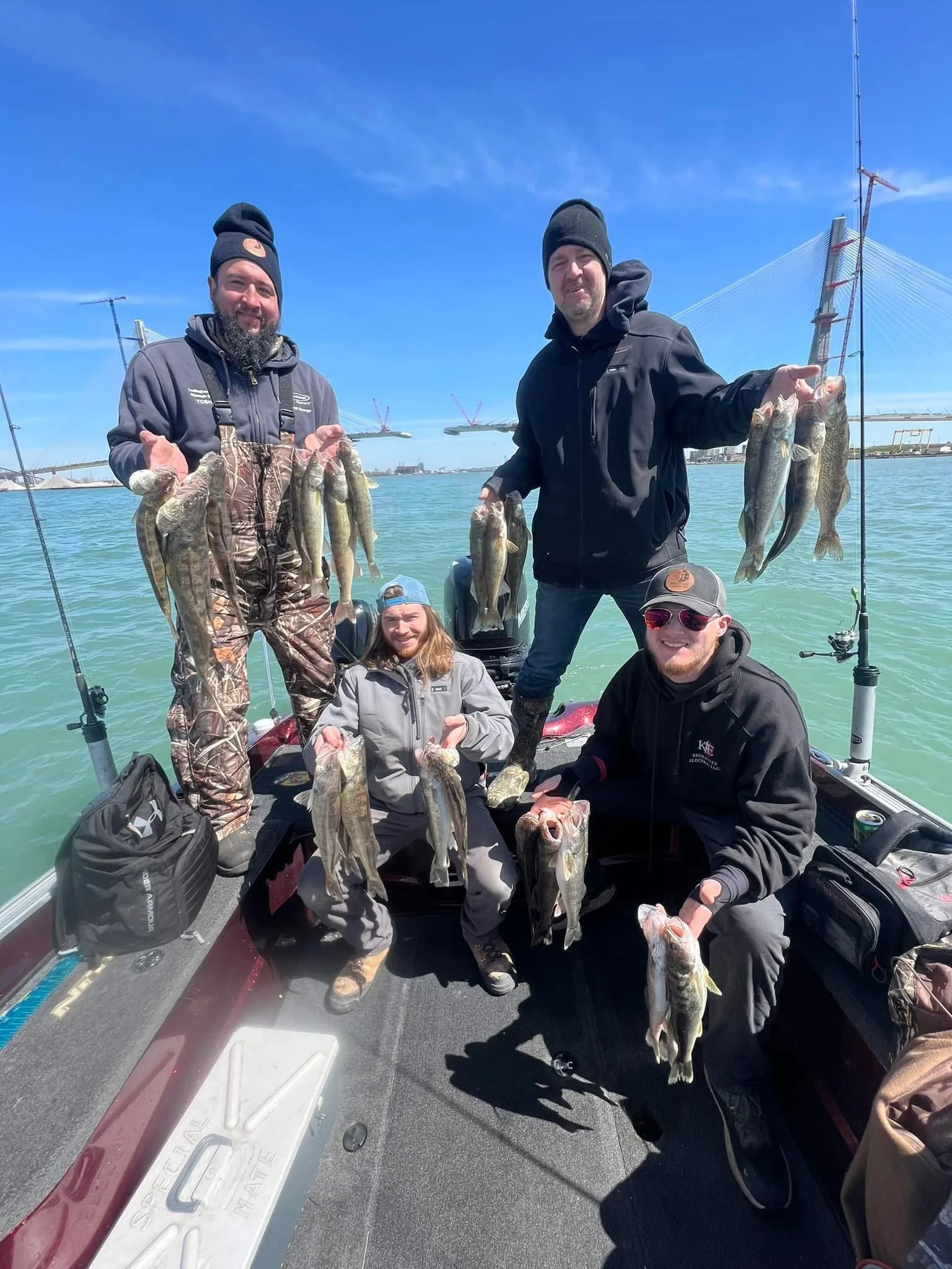 Four people on a boat holding up freshly caught fish, with a bridge and blue sky in the background.