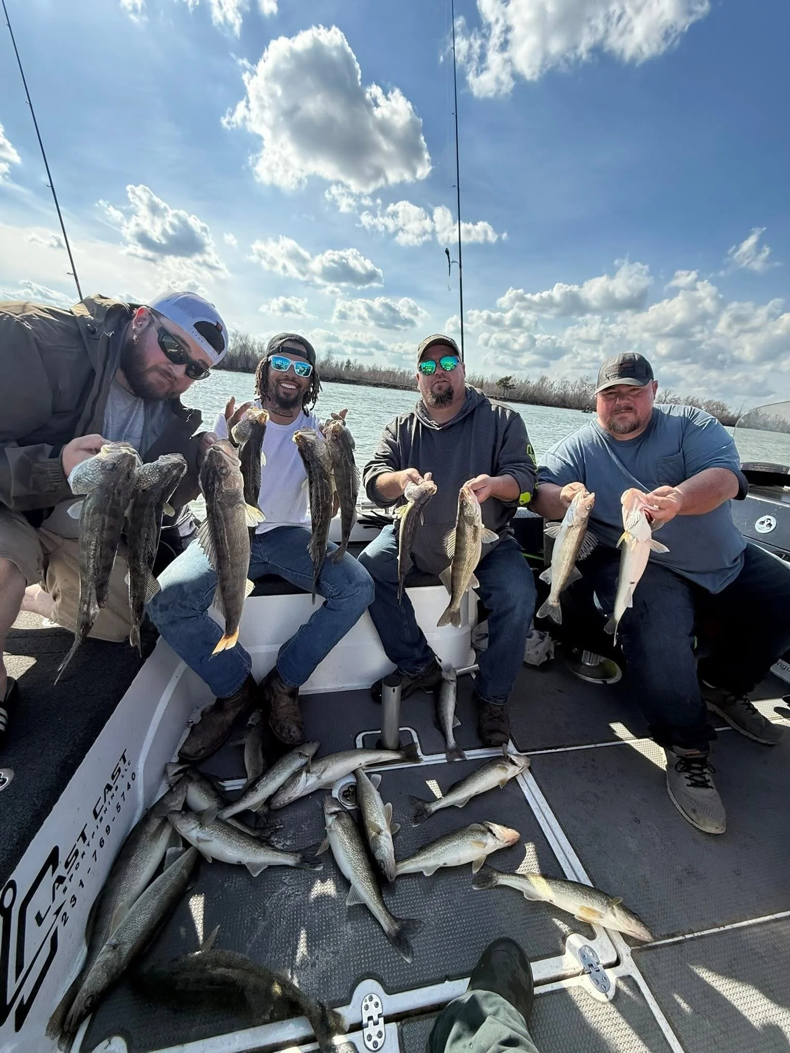 Four men on a boat holding large fish they caught, with a sky filled with clouds in the background.