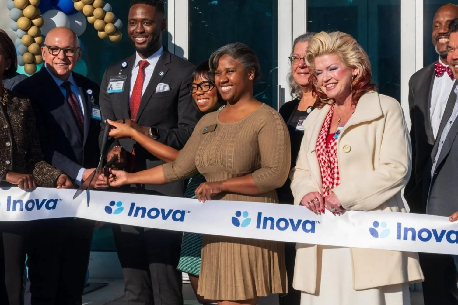 Margaret Franklin with a group of diverse people at a ribbon-cutting ceremony for Inova, smiling and holding scissors, with a ribbon that reads 'Inova'.