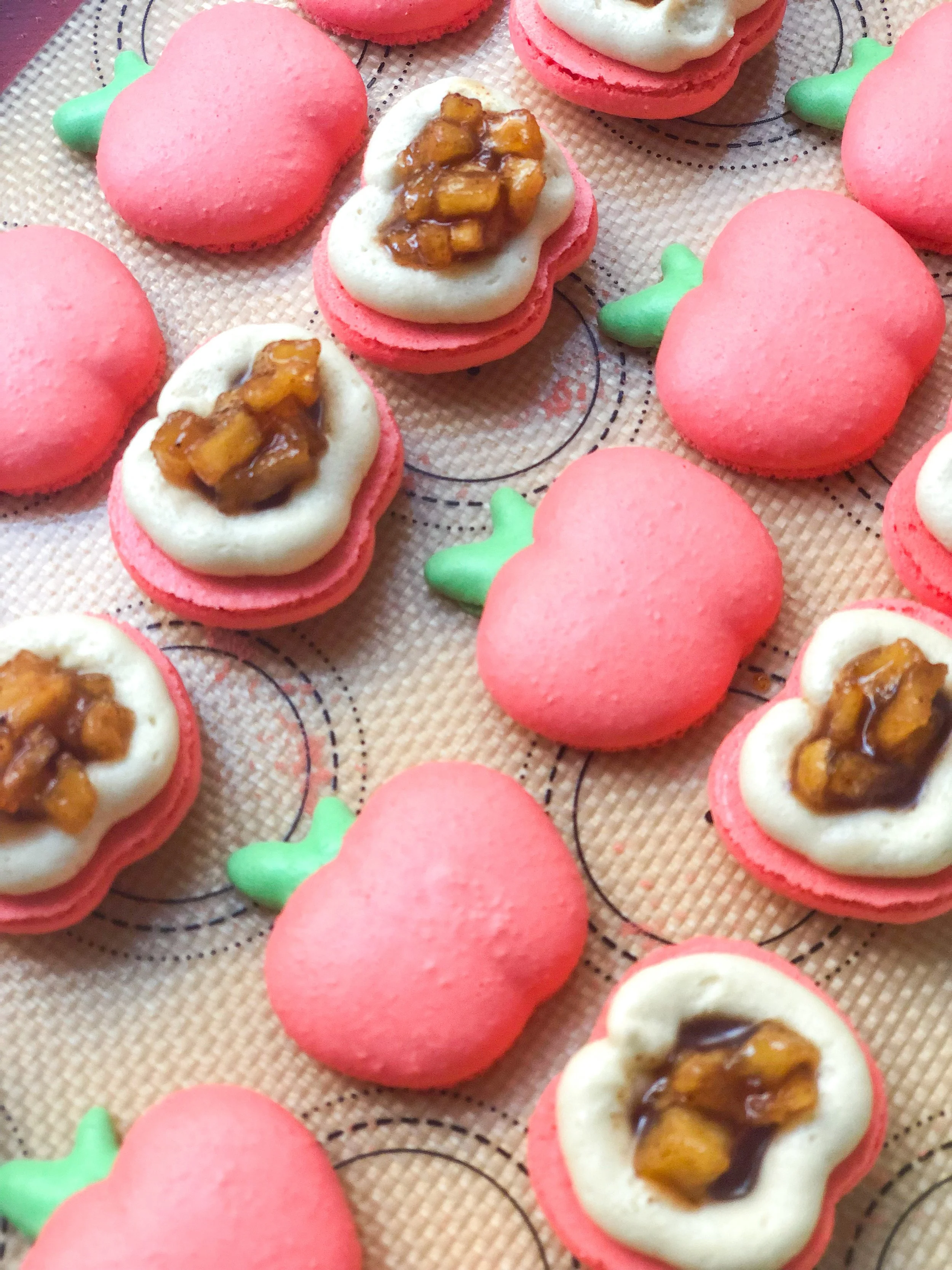 Close-up of strawberry-shaped and heart-shaped cookies decorated with pink, white, and green icing, some topped with caramel and nut clusters.