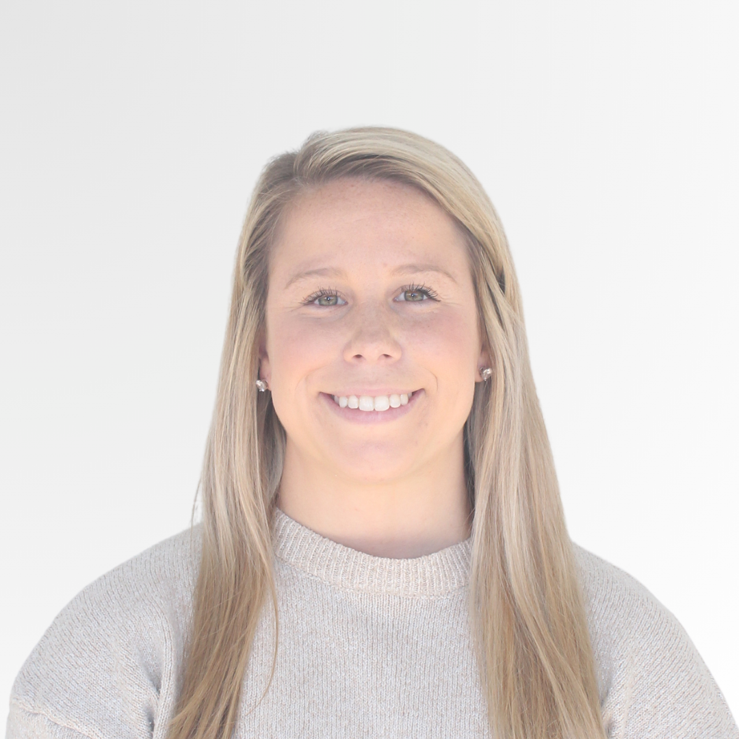 A young woman with long blonde hair smiling at the camera, wearing a beige sweater and earrings, against a plain white background.