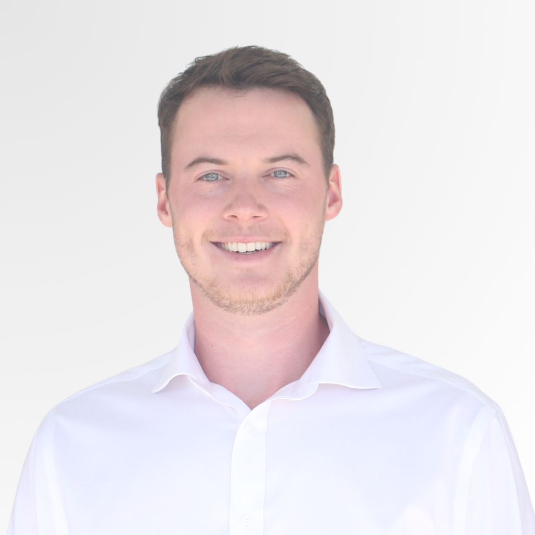 Headshot of a smiling young man with short brown hair, blue eyes, wearing a white dress shirt, against a white background.