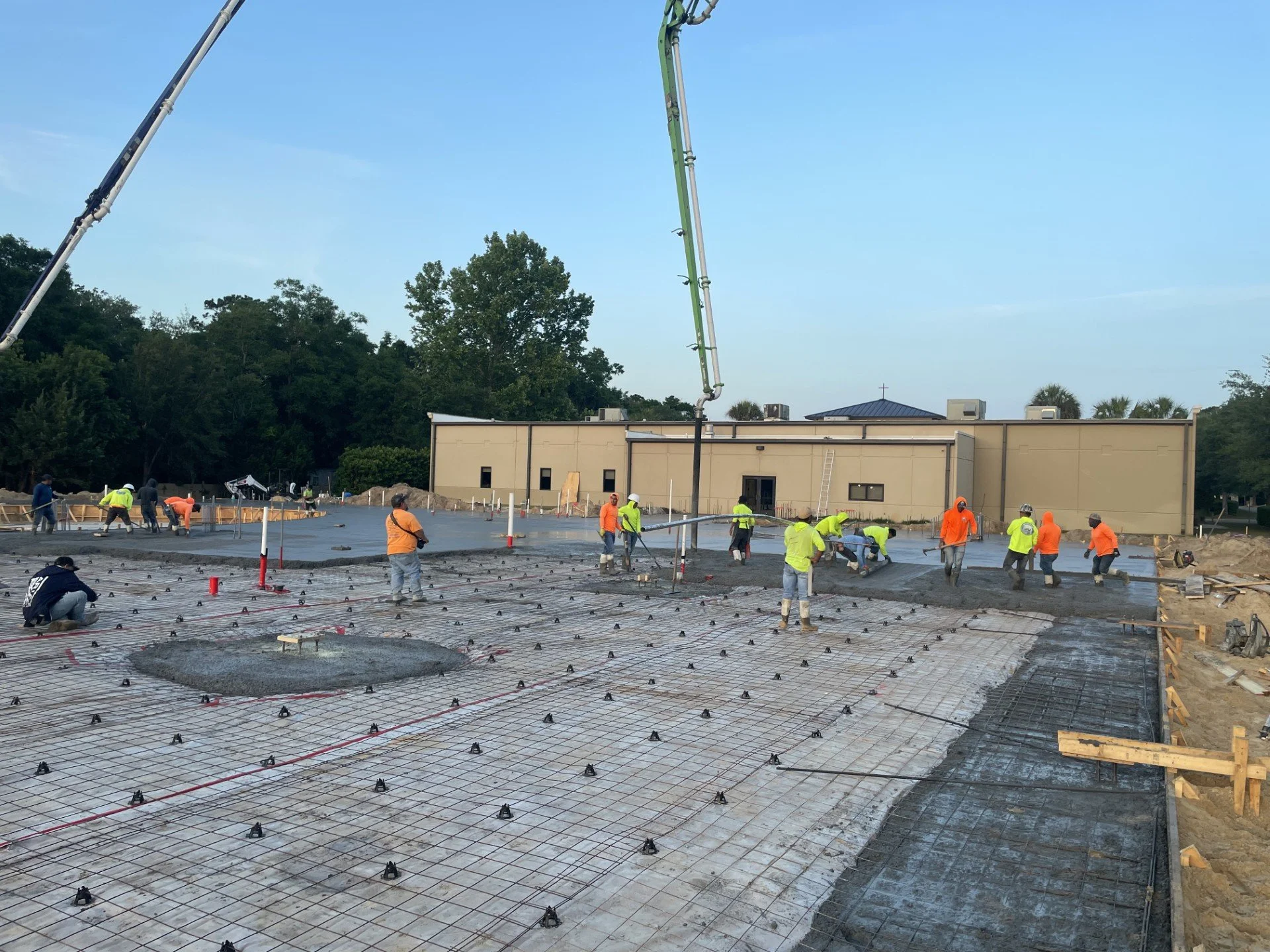 Construction workers pour concrete on a building site with a building in the background and a crane overhead.