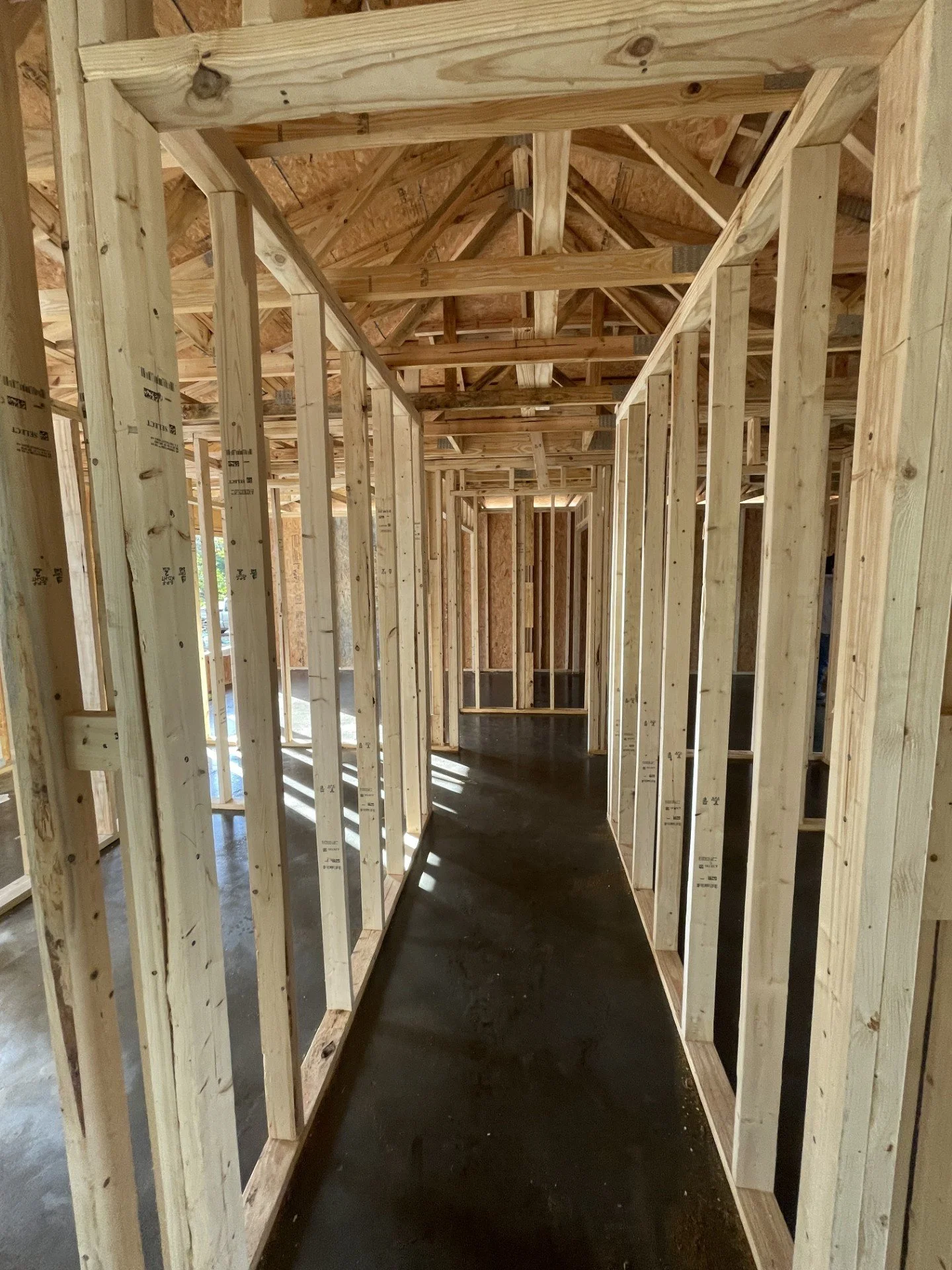 Interior view of a house under construction showing wooden framing, walls, and ceiling structure.