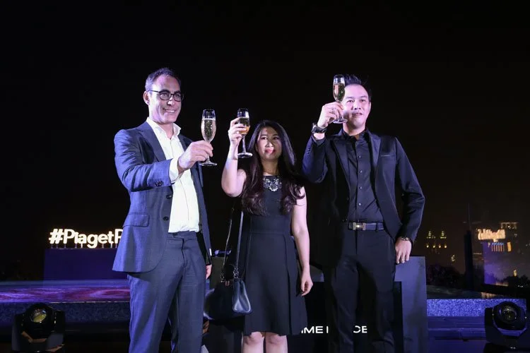 Three people in formal attire holding glasses of champagne, celebrating outdoors at night.