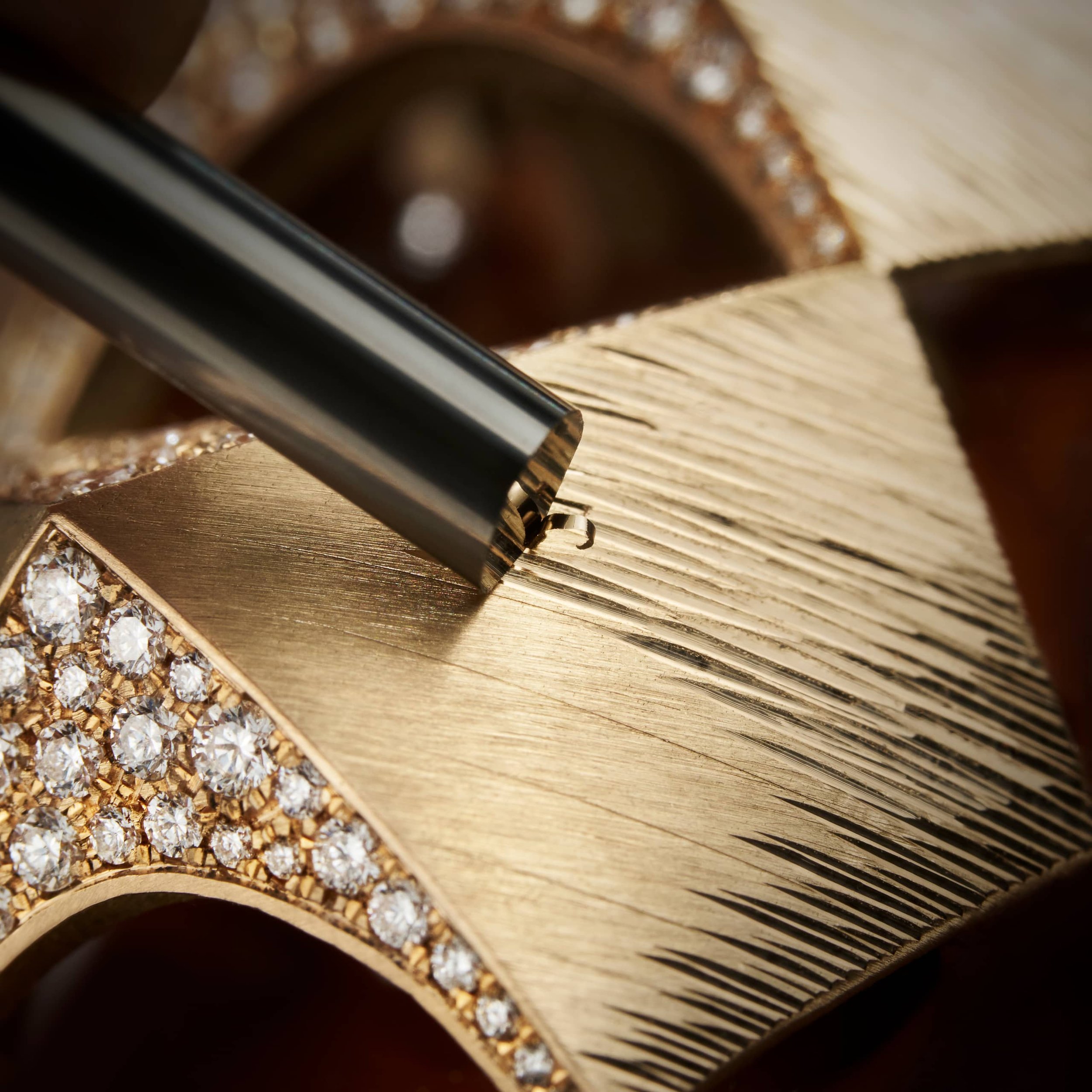 A close-up of a gold jewelry piece with diamonds being engraved or decorated with a precision tool.