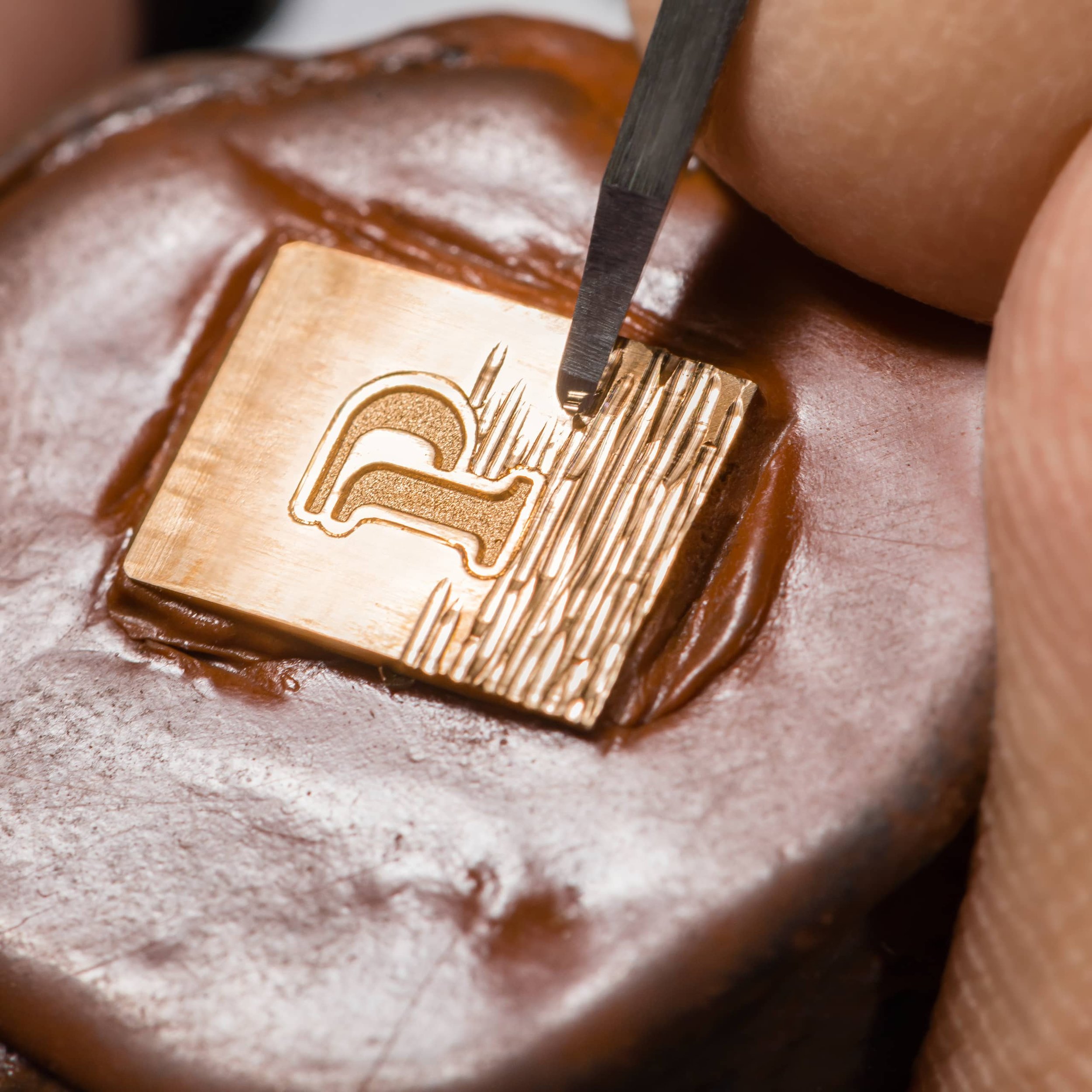 Close-up of a gold stamping die with a design being pressed into a piece of metal with a tool.